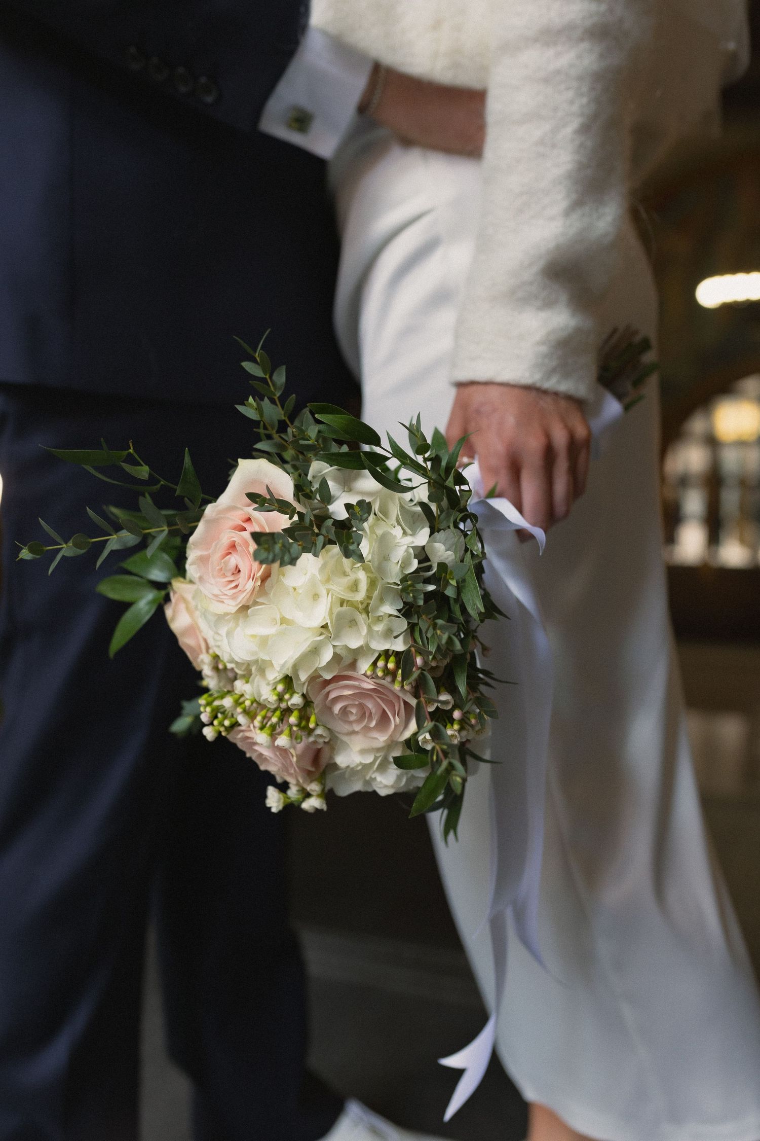 Elegant wedding bouquet with pink and white roses and greenery against formal attire.