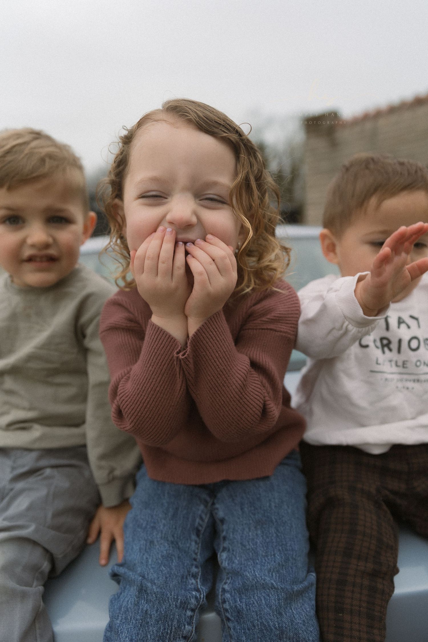 Small children sitting on car trunk sharing a candid moment, main focus on toddler girl giggling captured in a film-like editing