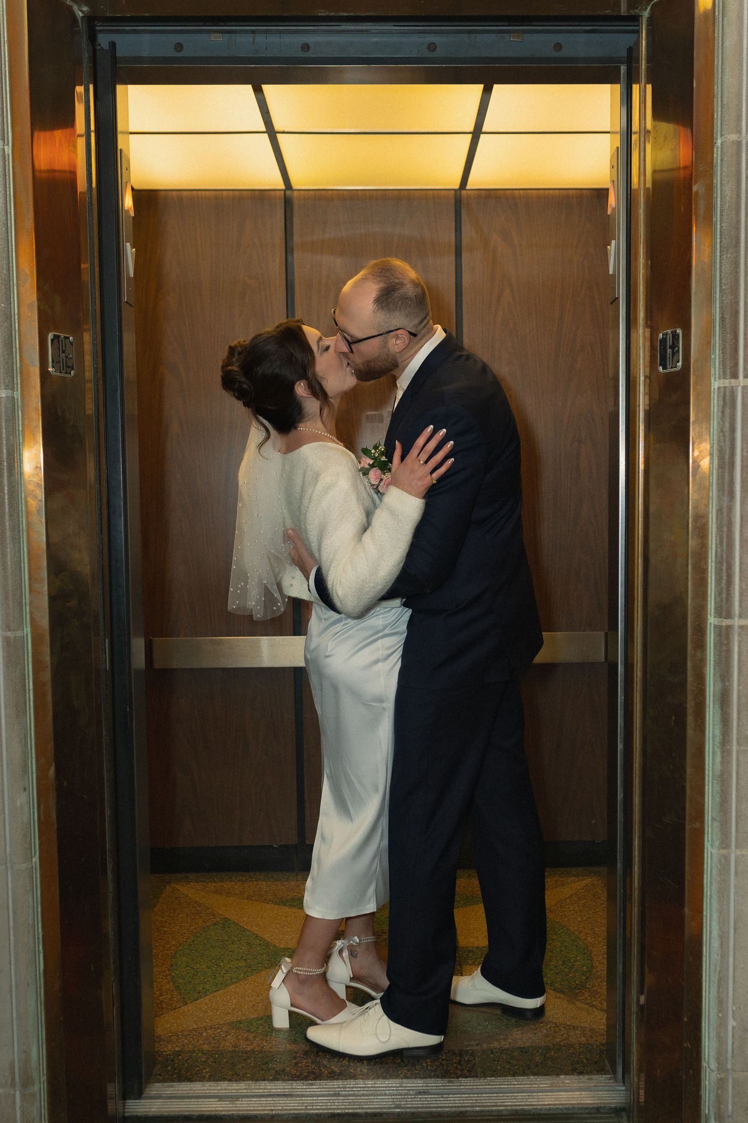 Romantic moment between newlyweds in gold-lit elevator.