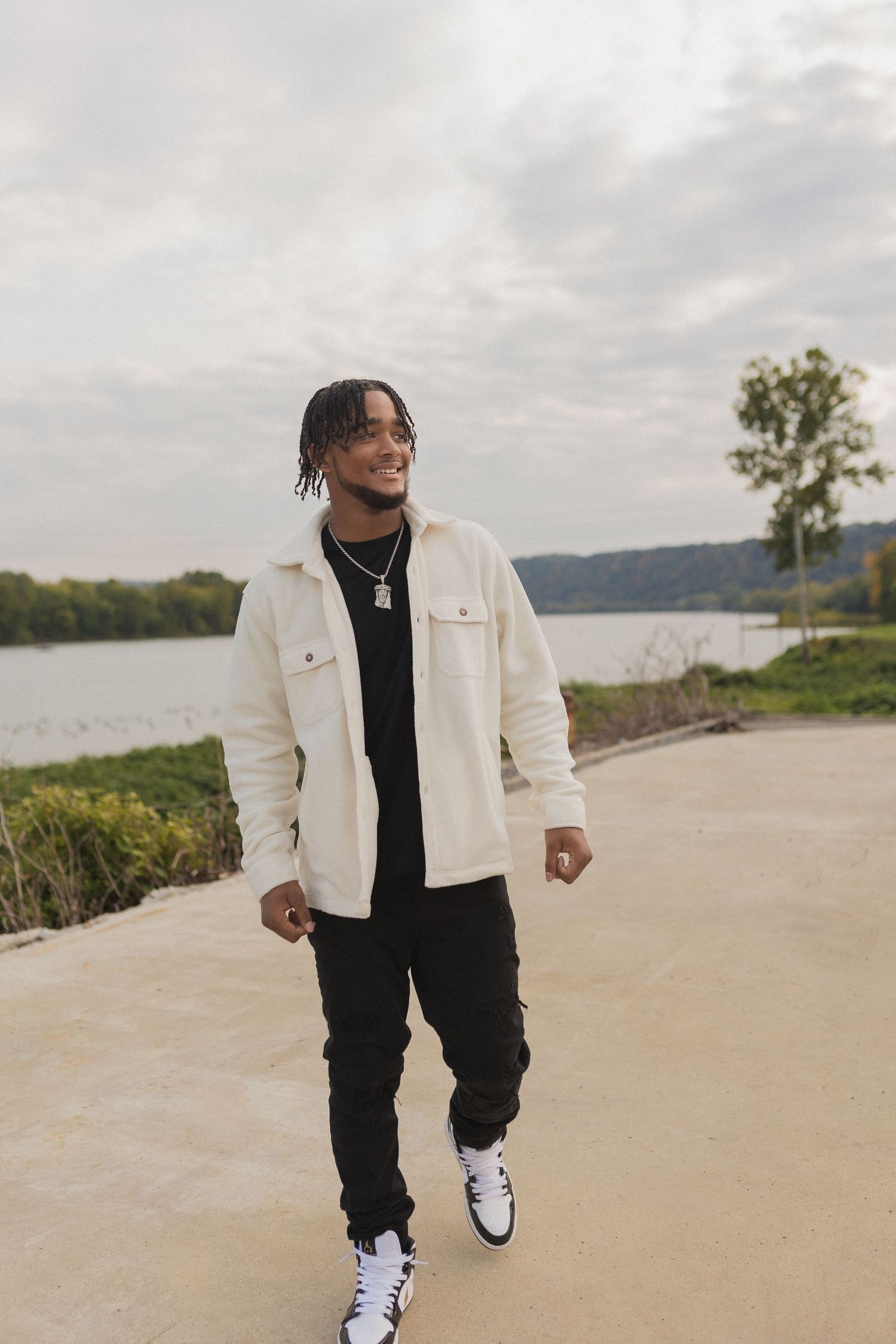 Person walking on path near lake wearing white denim jacket and black pants with white sneakers.