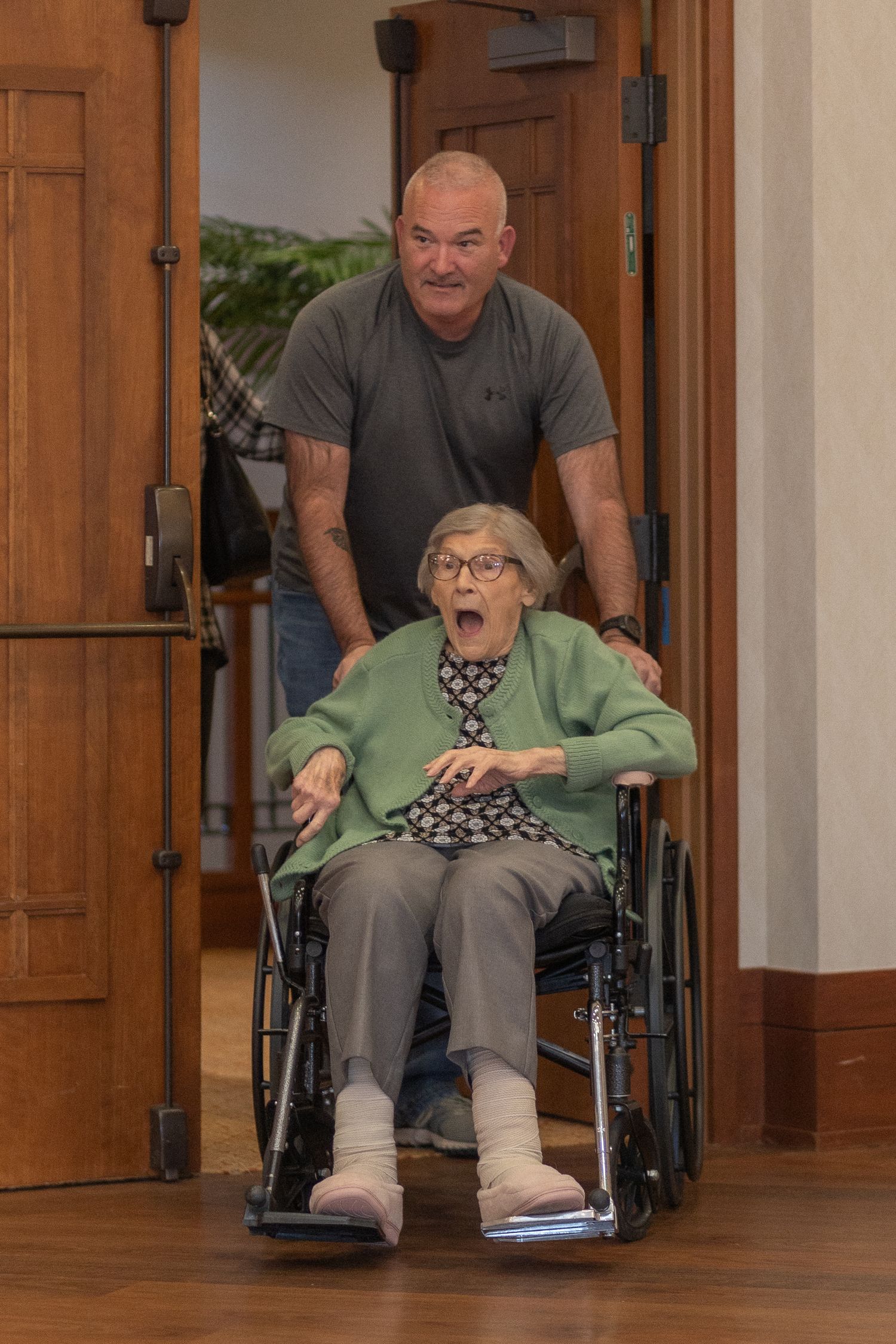 A joyful moment captured as someone pushes a wheelchair through wooden doors.