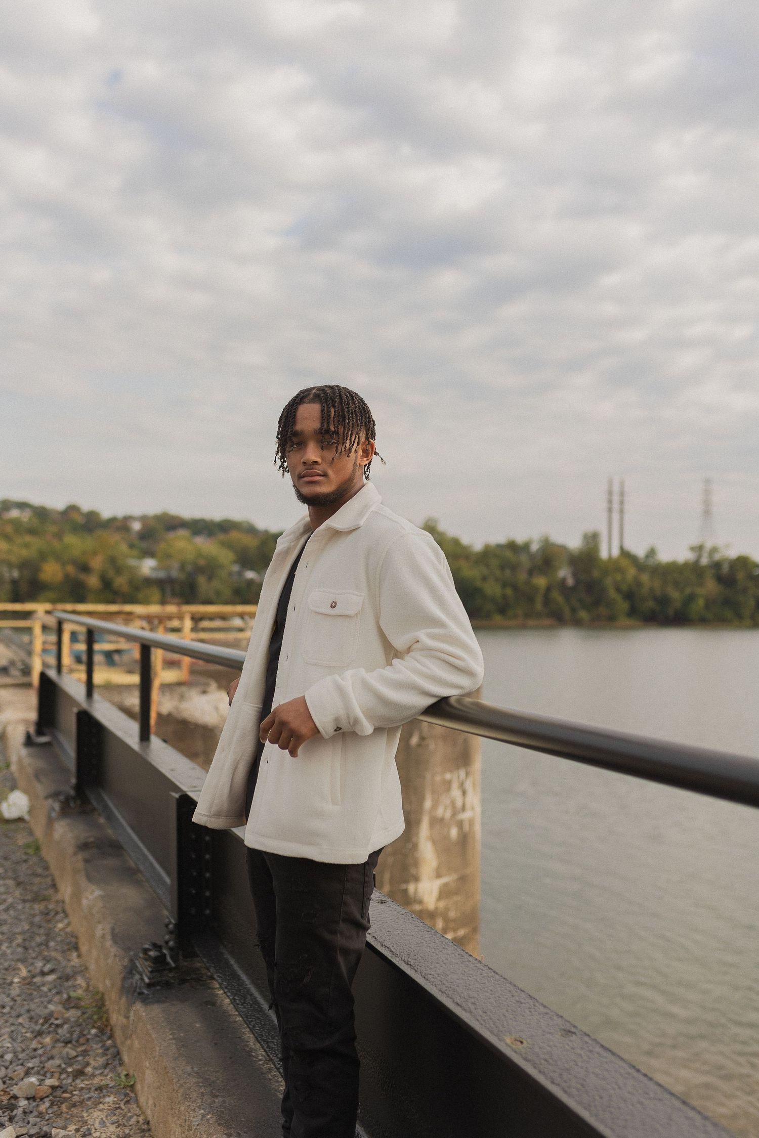 Person in white jacket stands by railing overlooking water on overcast day.