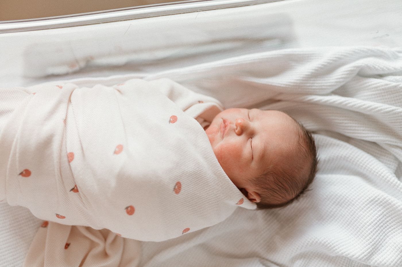 Newborn swaddled in soft white blanket with peach dots, cozy hospital session with fresh 48 vibes and peaceful film like tones.