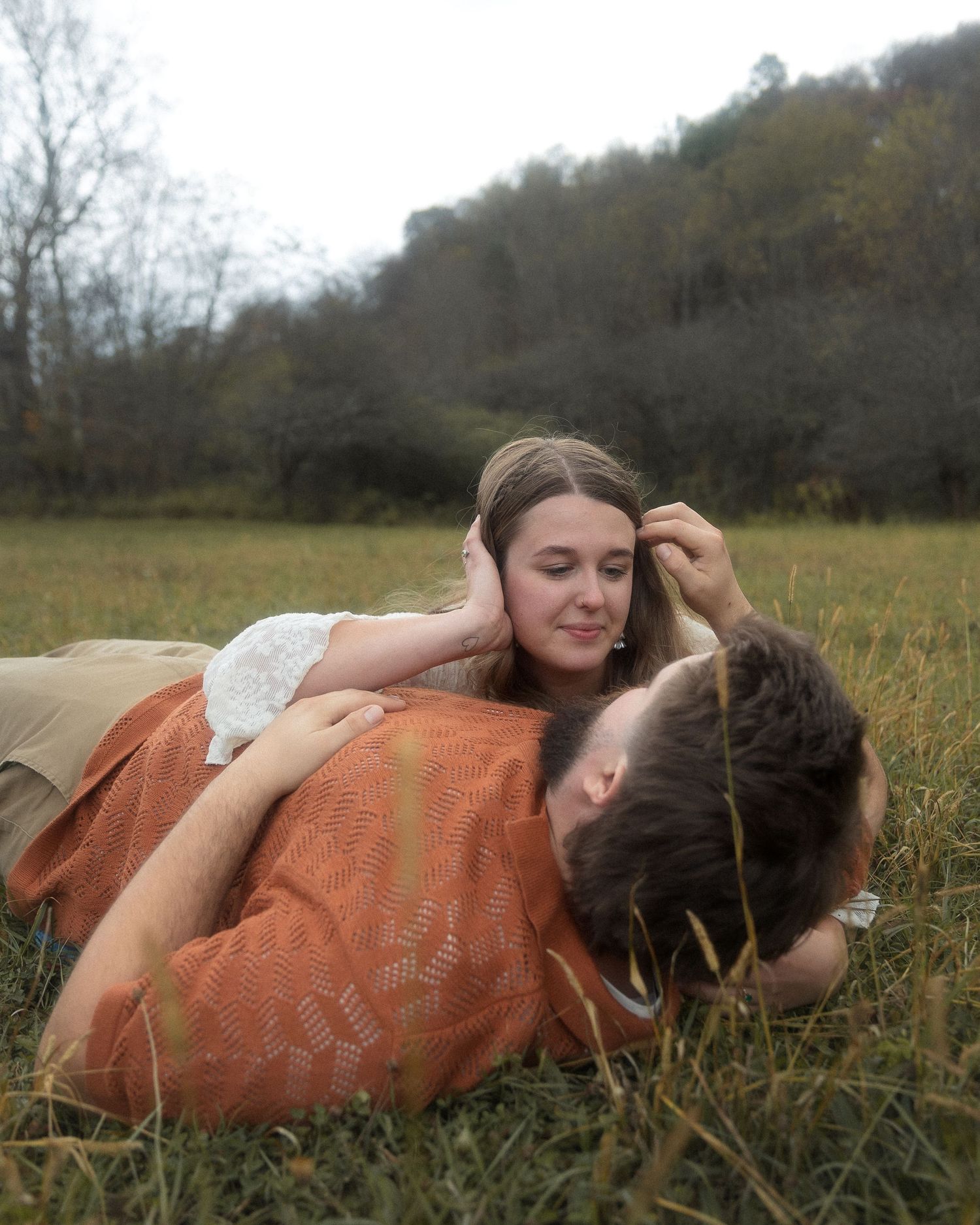 Two people lying together in a grassy field on an autumn day with orange blanket.