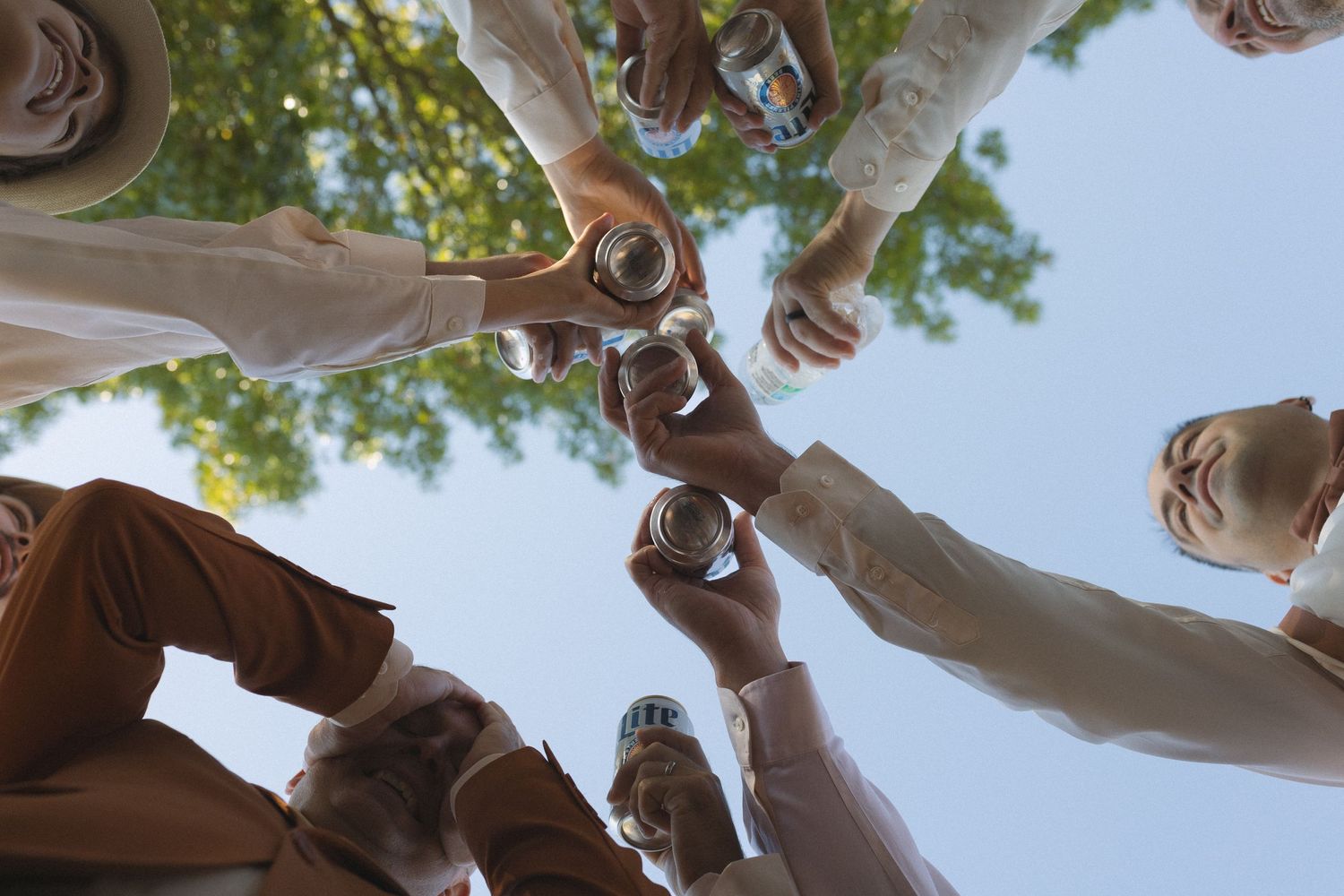 Low angle view of wedding party toasting with champagne glasses against blue sky.