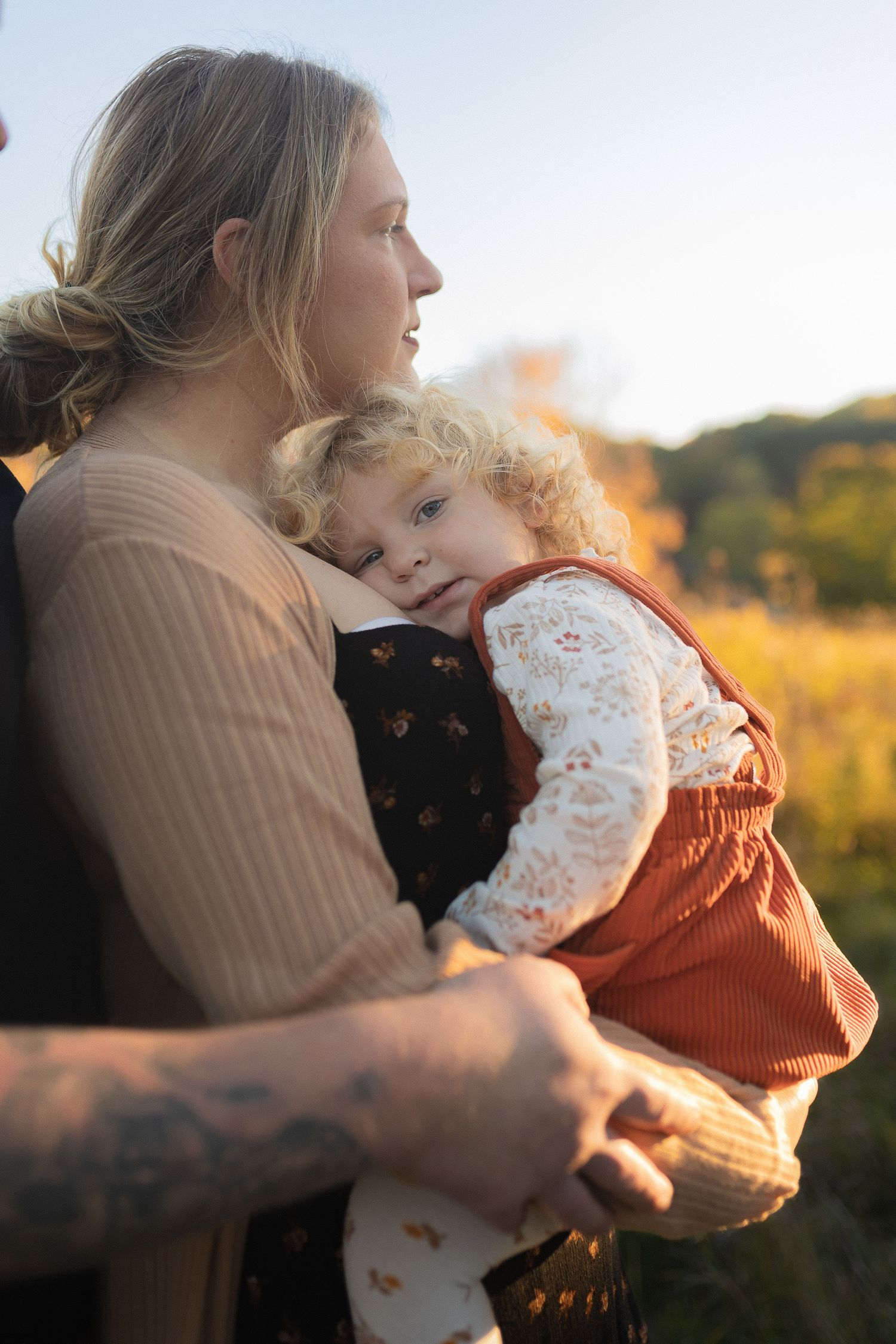 A gentle embrace captured in warm sunlight with fall foliage in the background.