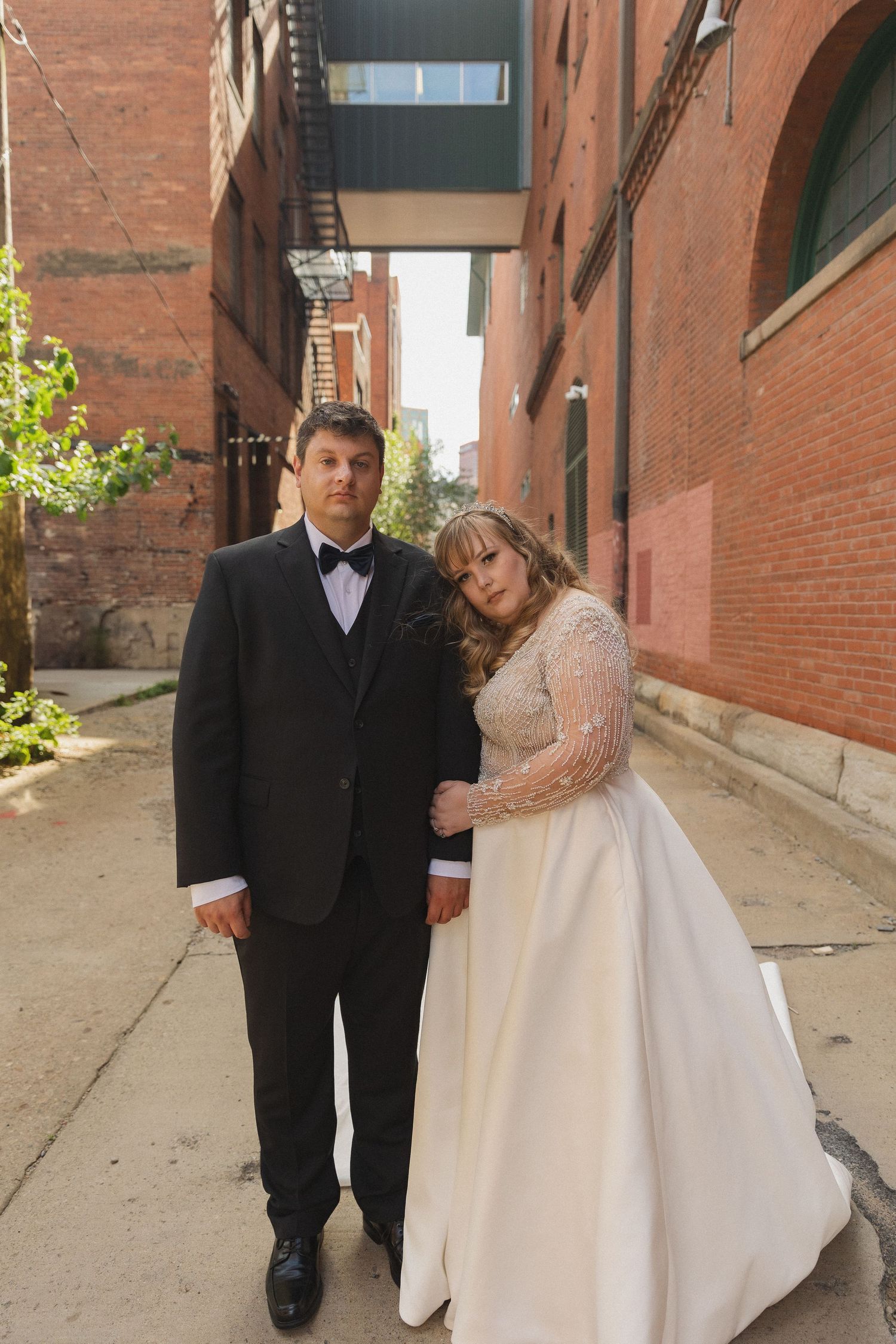 A wedding couple posing in an urban alley with red brick walls.