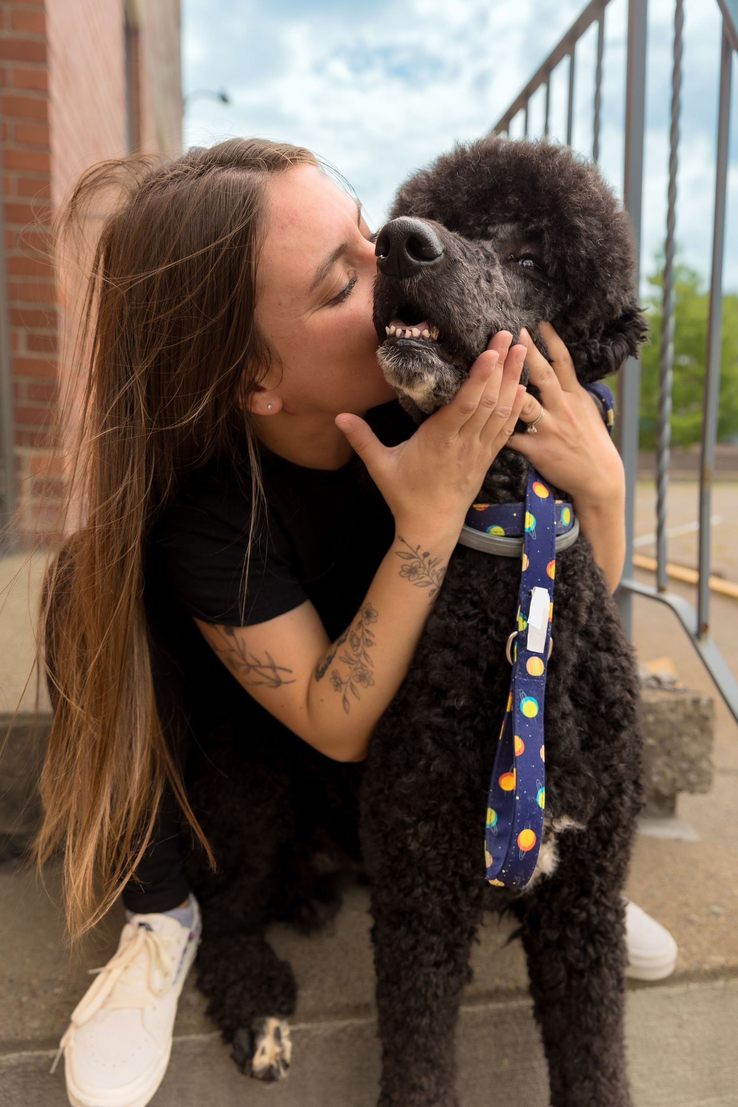 A heartwarming moment between a black poodle and its owner sharing an affectionate kiss outdoors.