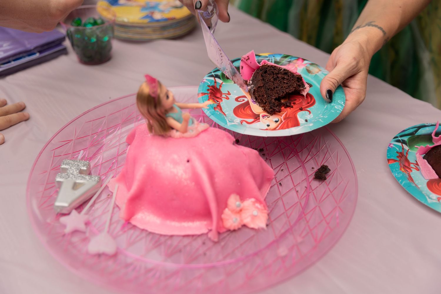 Pink princess dress cake and chocolate cupcake on pink plates at a party.