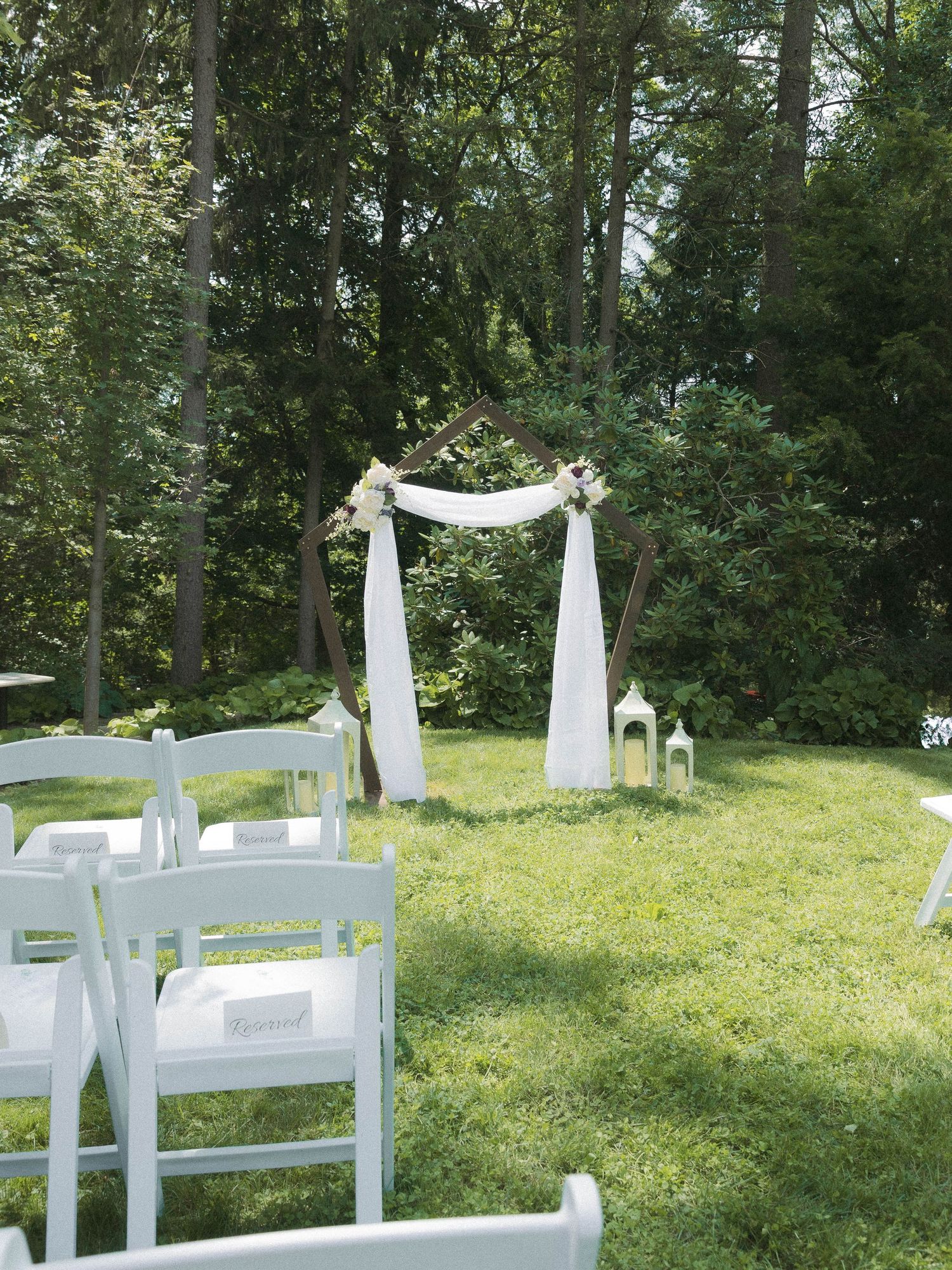 White wooden ceremony benches and archway decorated with flowing fabric set up on a grassy hillside for an outdoor wedding.
