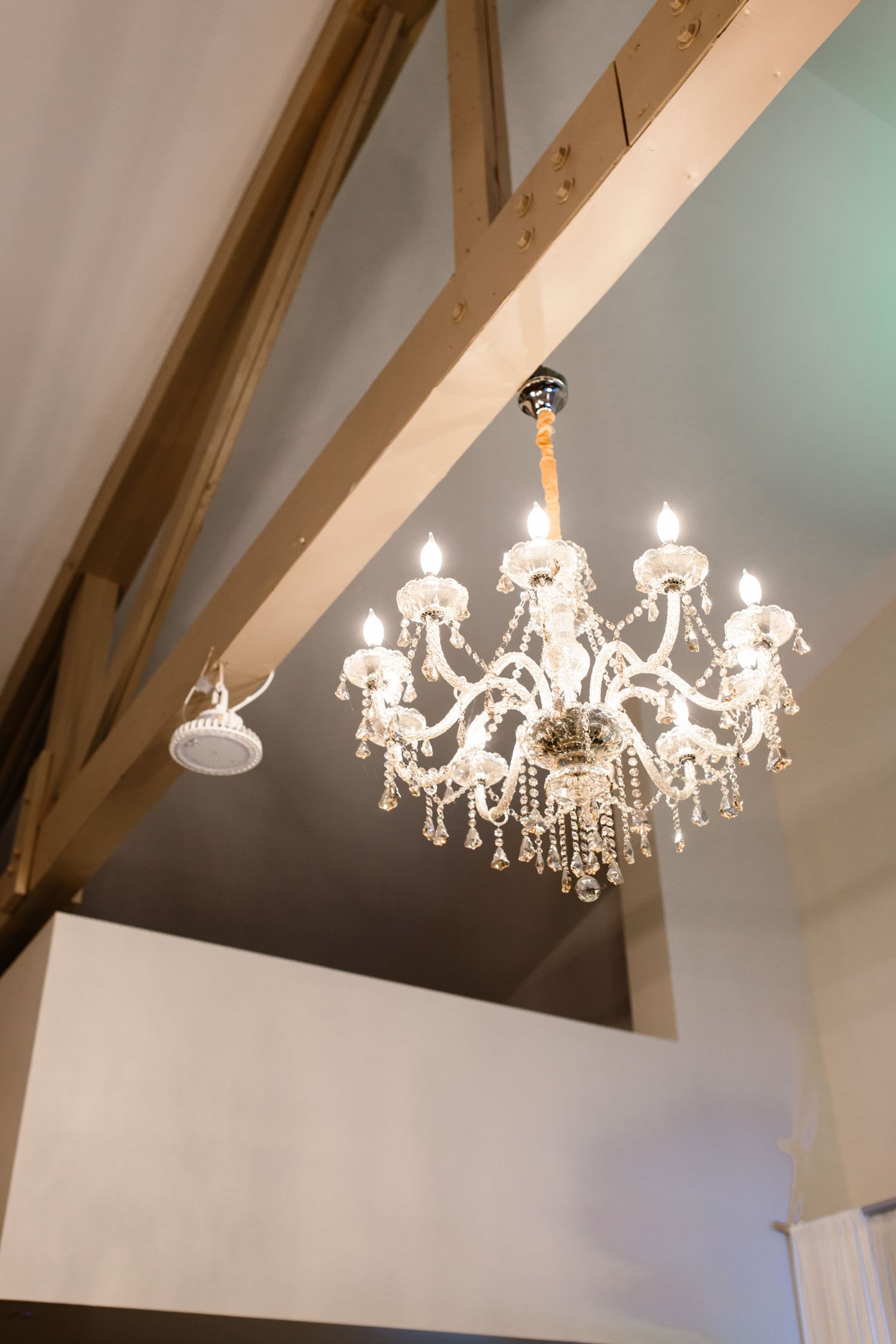 Stunning crystal chandelier hanging from rustic wooden beamed ceiling inside a beautiful wedding venue.