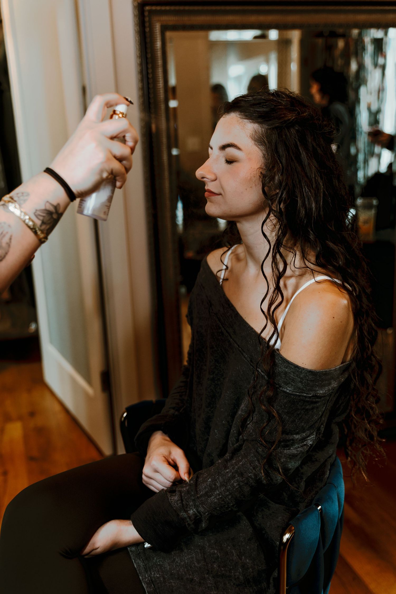 Bride getting makeup applied by a stylist while seated in a chair during wedding day preparations.