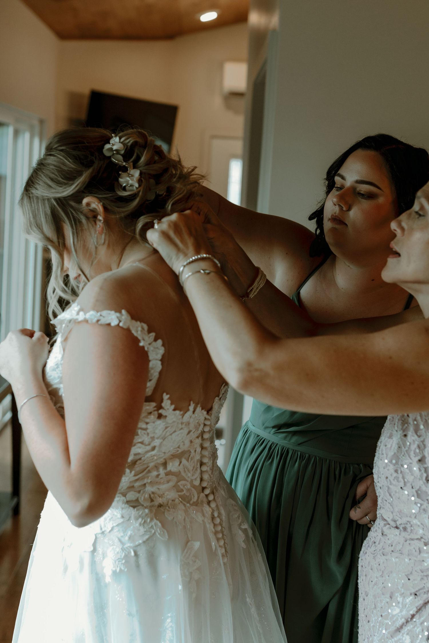 Bridesmaids helping bride fasten her lace wedding dress before the ceremony.