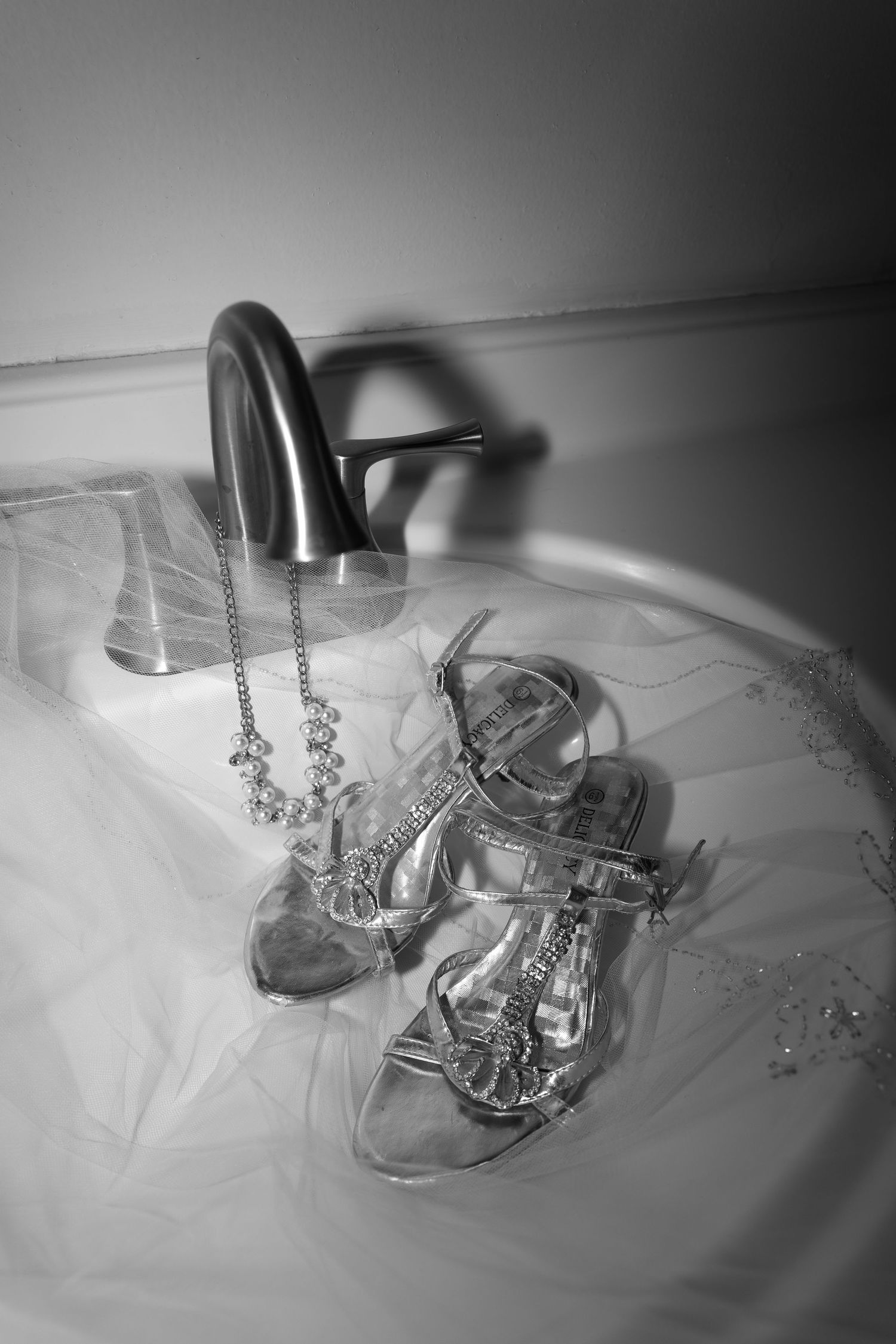 Black and white photo of bridal heels, veil, and jewelry arranged elegantly in a bathtub near a faucet.