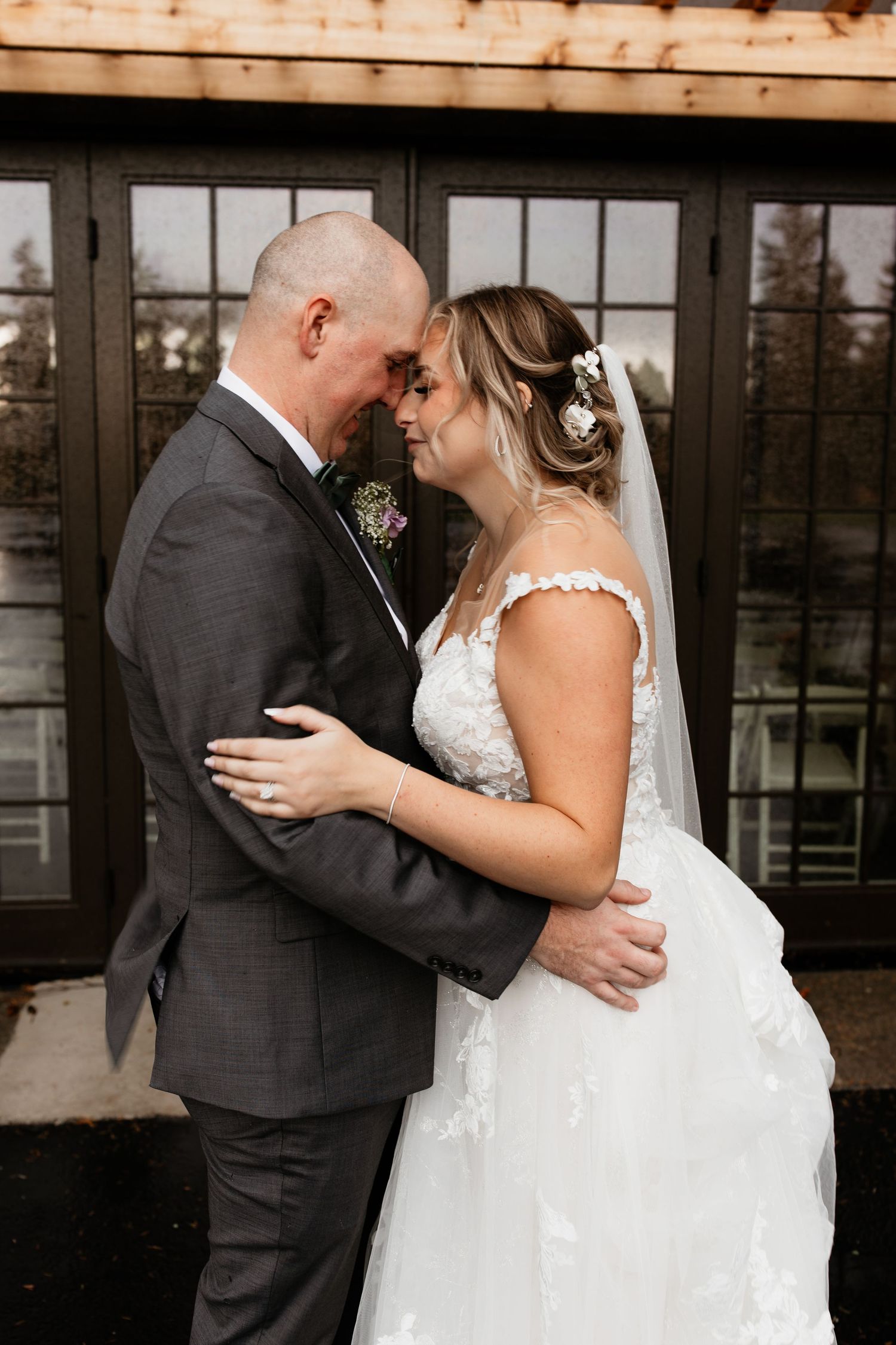 Bride and groom touching foreheads romantically while embracing outside their wedding venue.