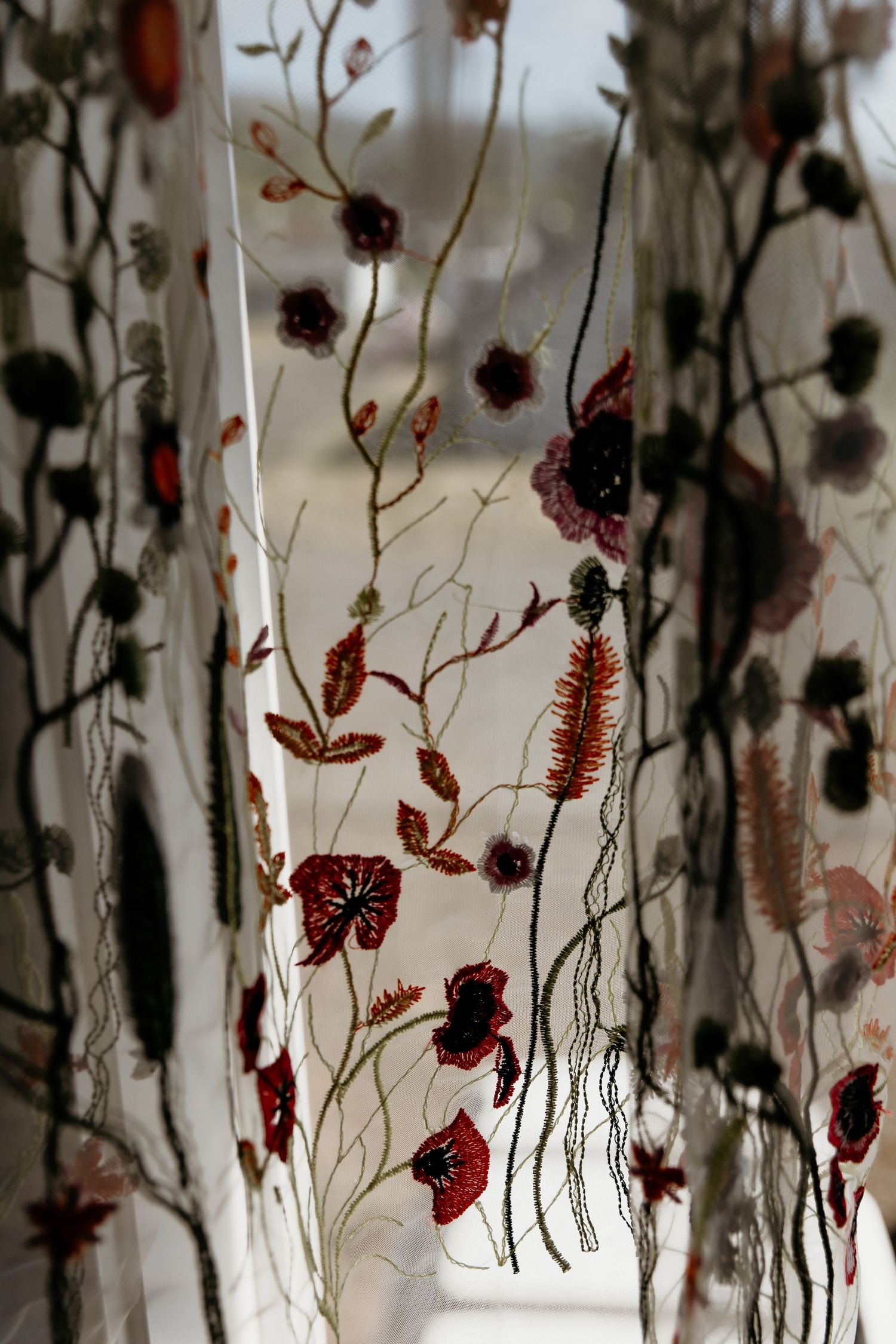 Sheer curtain with intricate floral embroidery featuring red poppies and wildflowers on delicate mesh fabric.