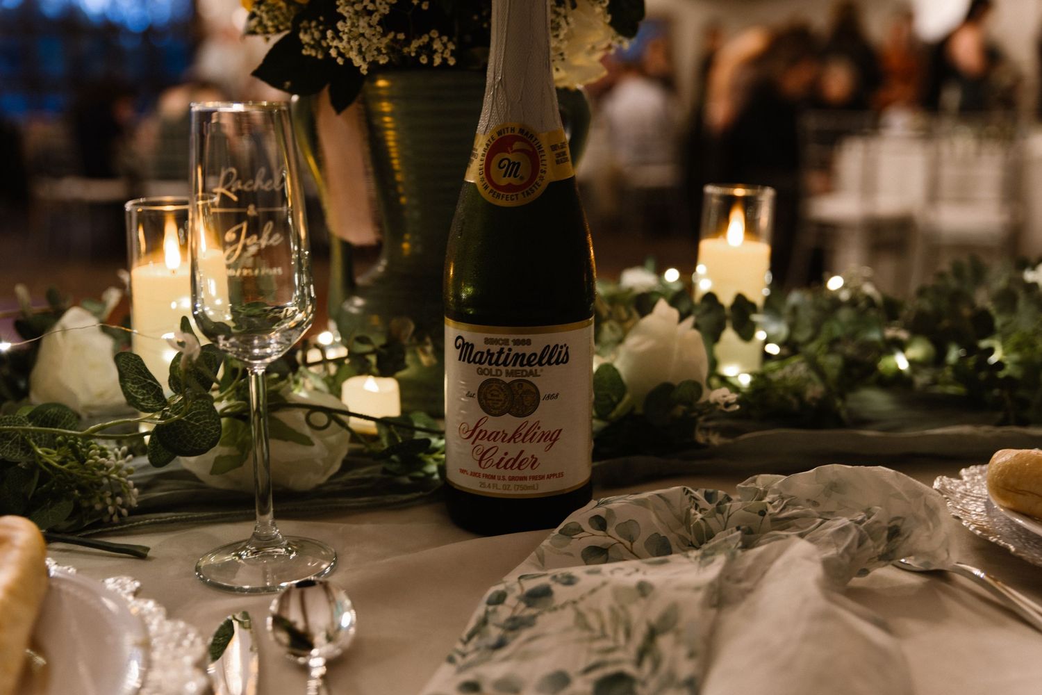Elegant wedding reception table with Martinellis sparkling cider, candles, and lush greenery centerpiece.