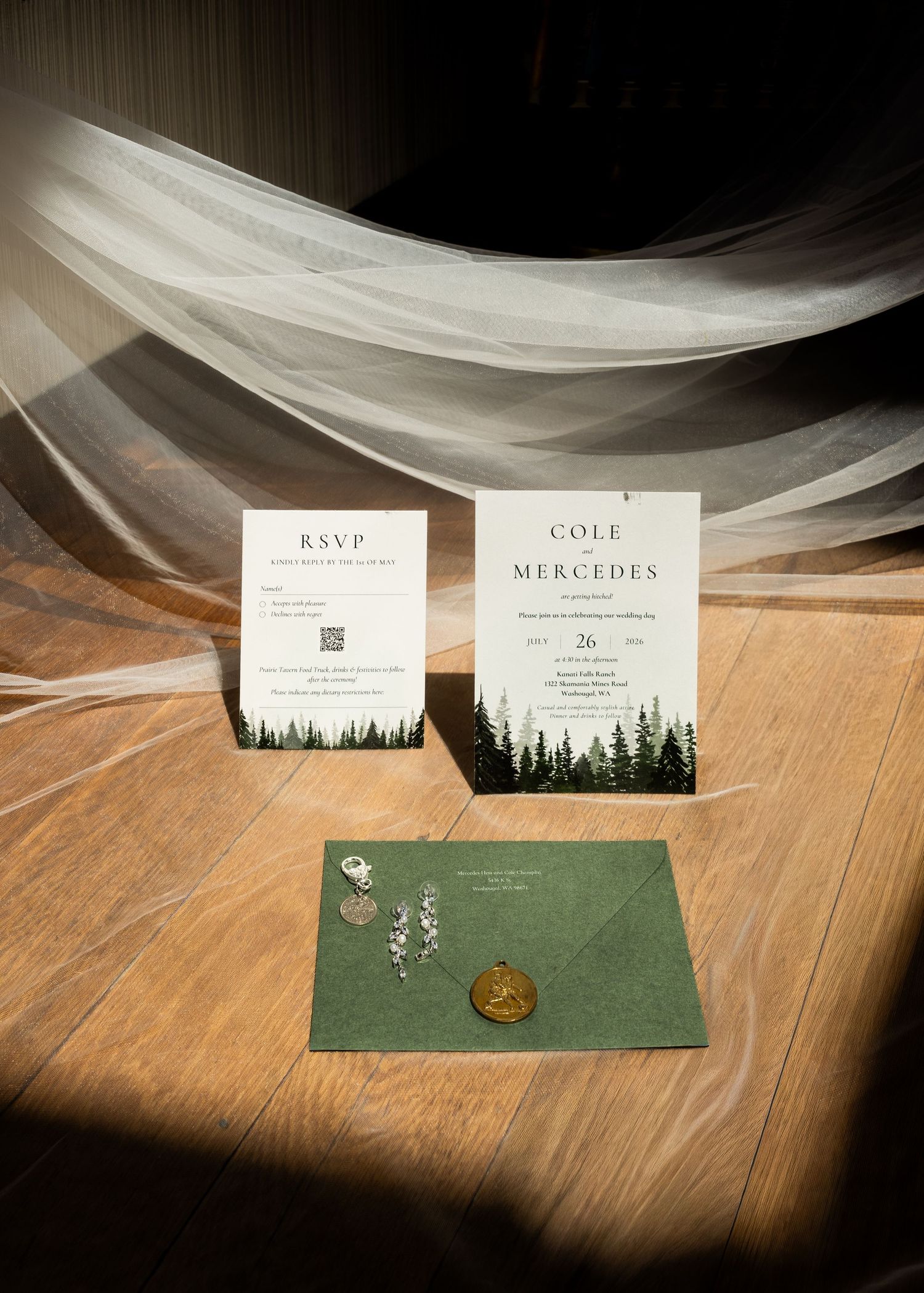 Elegant wedding invitation suite with forest pine tree design, green envelope with gold wax seal, and RSVP card on wood floor.