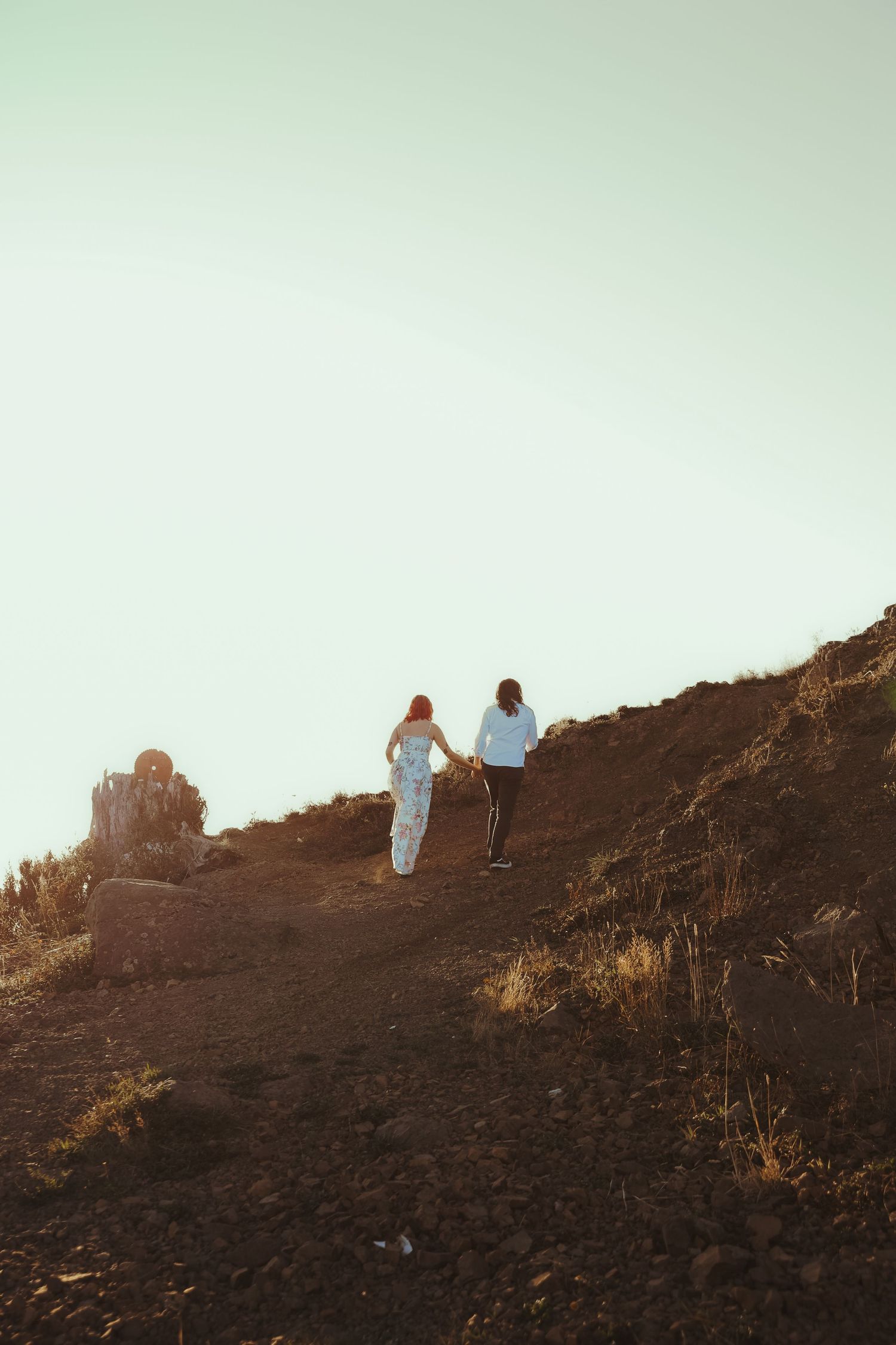 Two people walking up a rocky hillside trail at sunset with a clear sky backdrop.