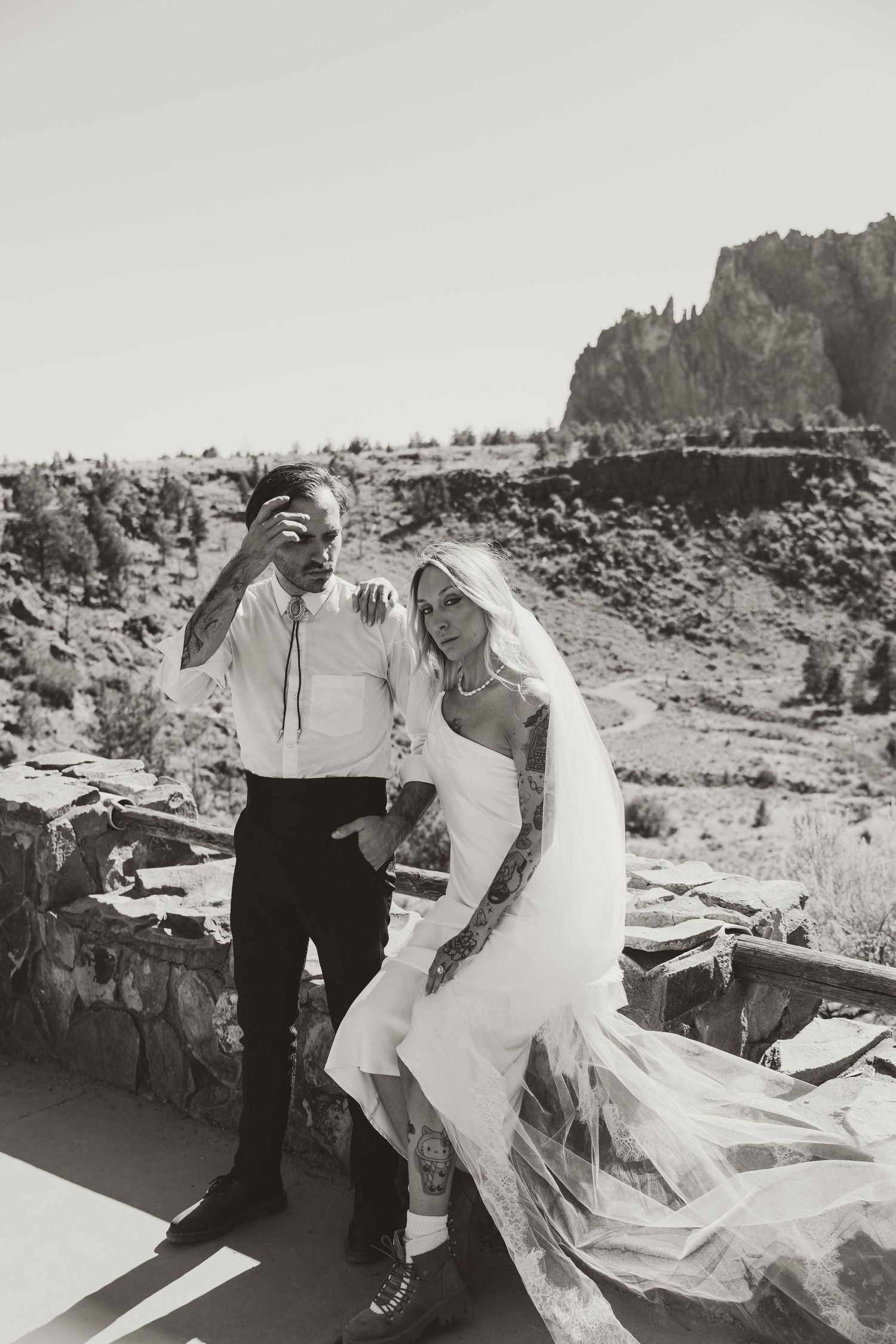 Black and white photo of bride and groom posing outdoors with rocky mountain landscape backdrop on their wedding day.