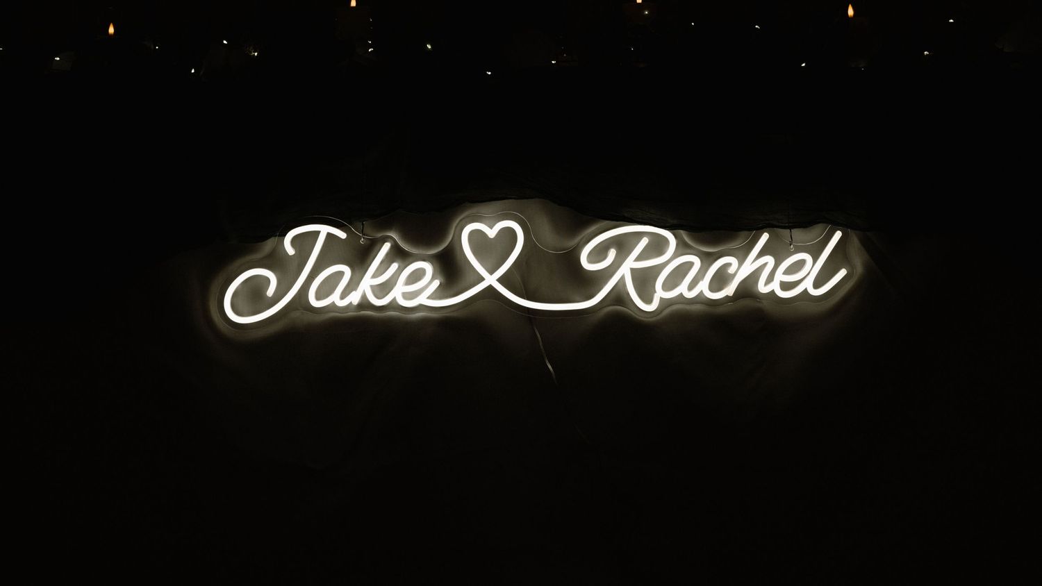 Glowing white neon sign reading Jake and Rachel with a heart, perfect for a wedding reception backdrop.