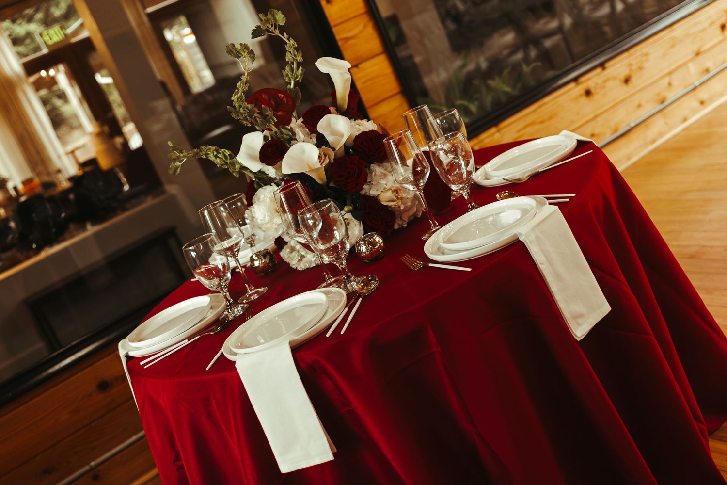 Elegant wedding reception table with red velvet tablecloth, white napkins, crystal glasses, and floral centerpiece.