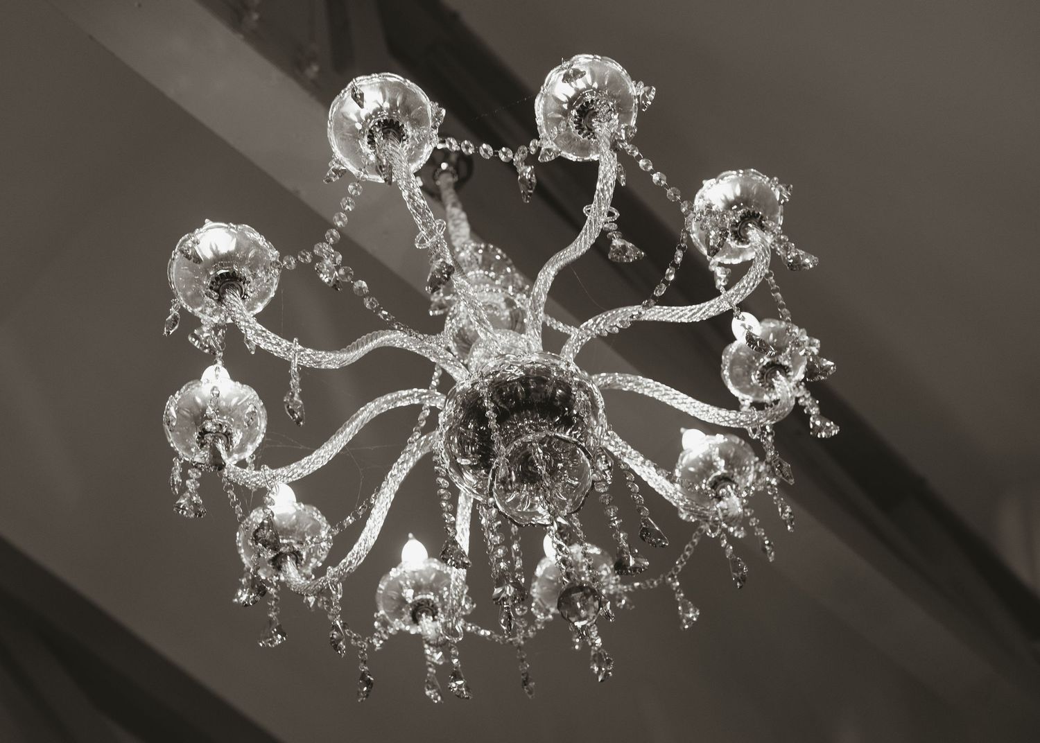 Elegant crystal chandelier with curved arms and dangling crystal accents, photographed from below against a dark ceiling.
