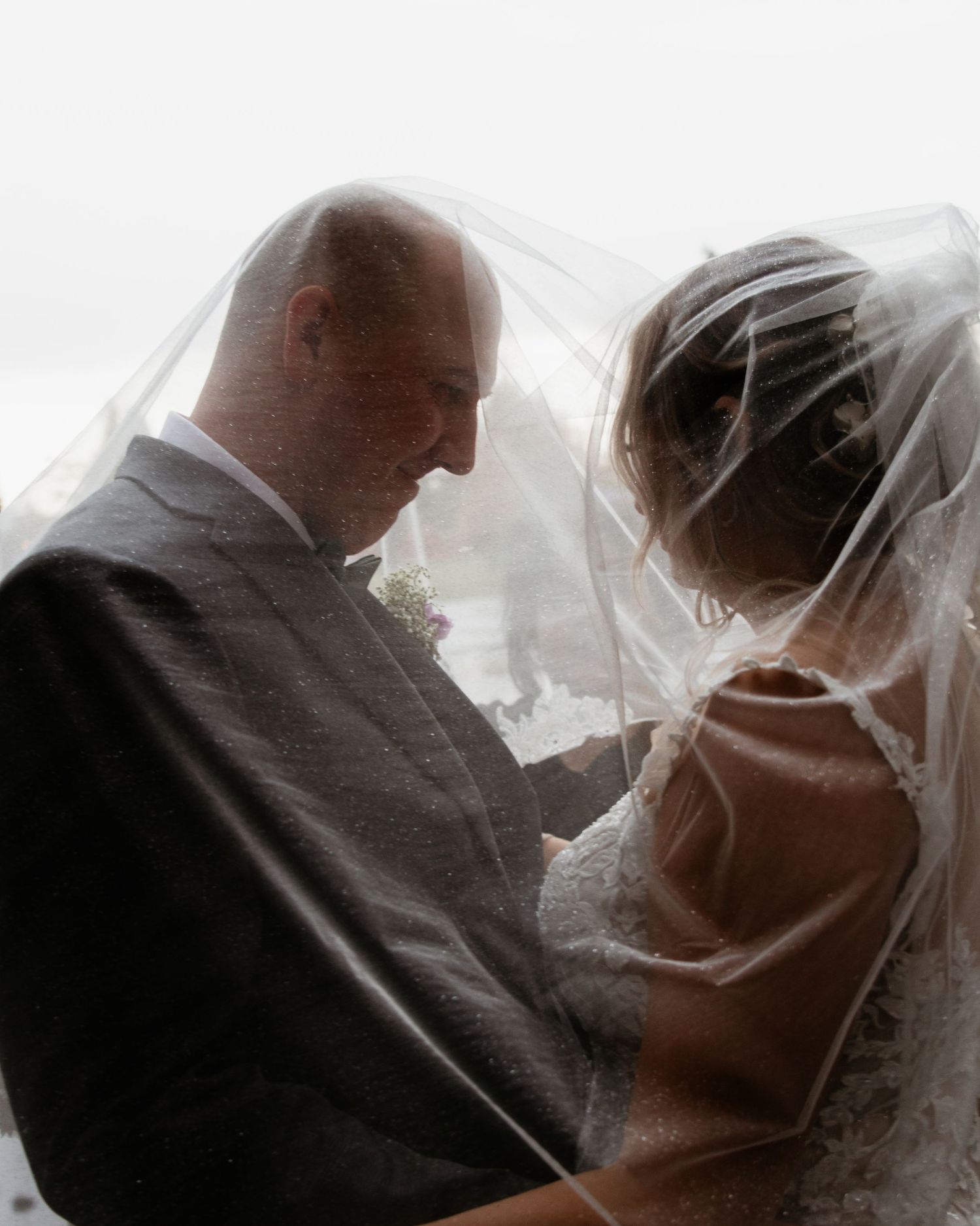 Romantic black and white photo of a bride and groom sharing an intimate moment under a wedding veil.