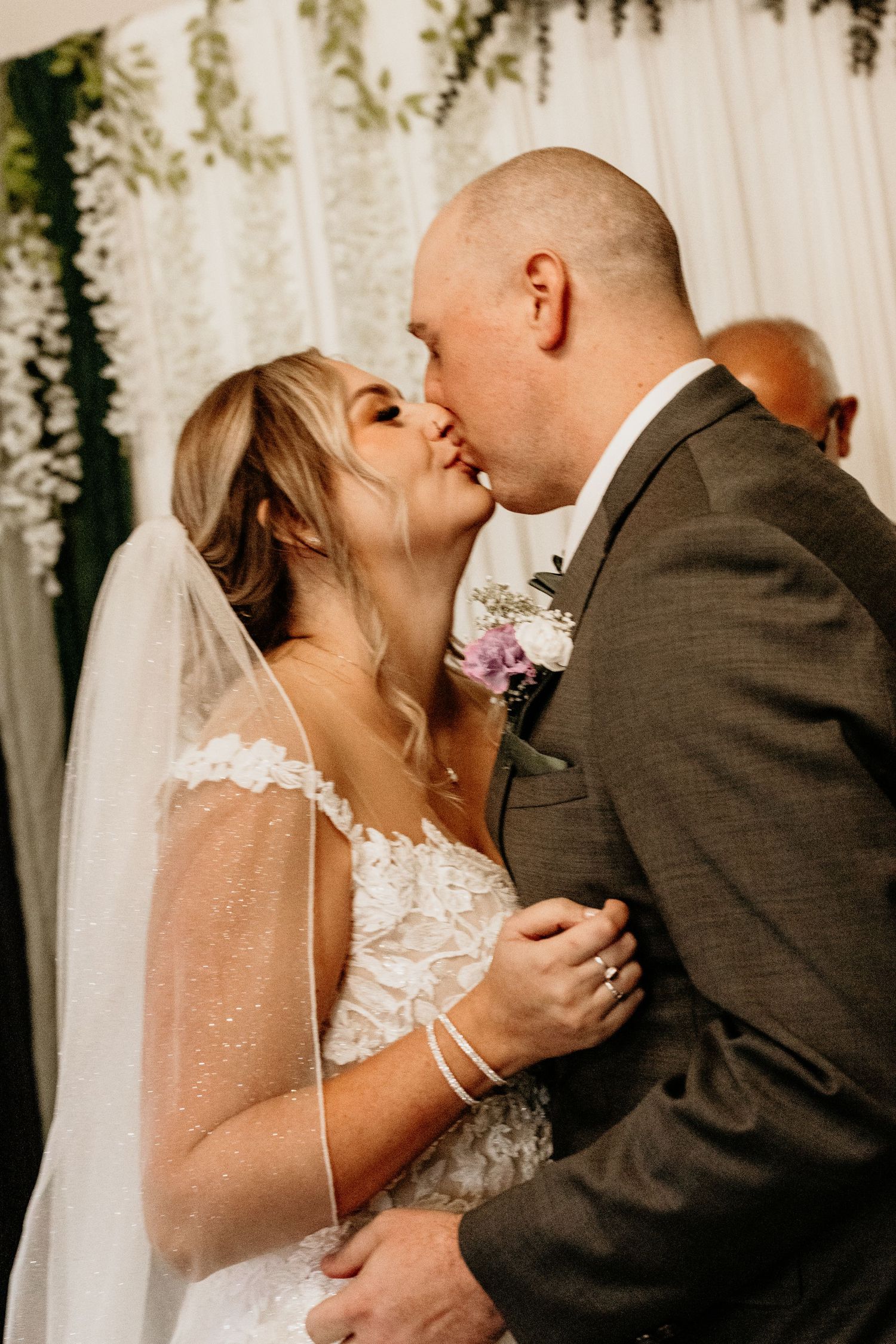 Bride and groom share first kiss at wedding altar decorated with white draping and greenery.