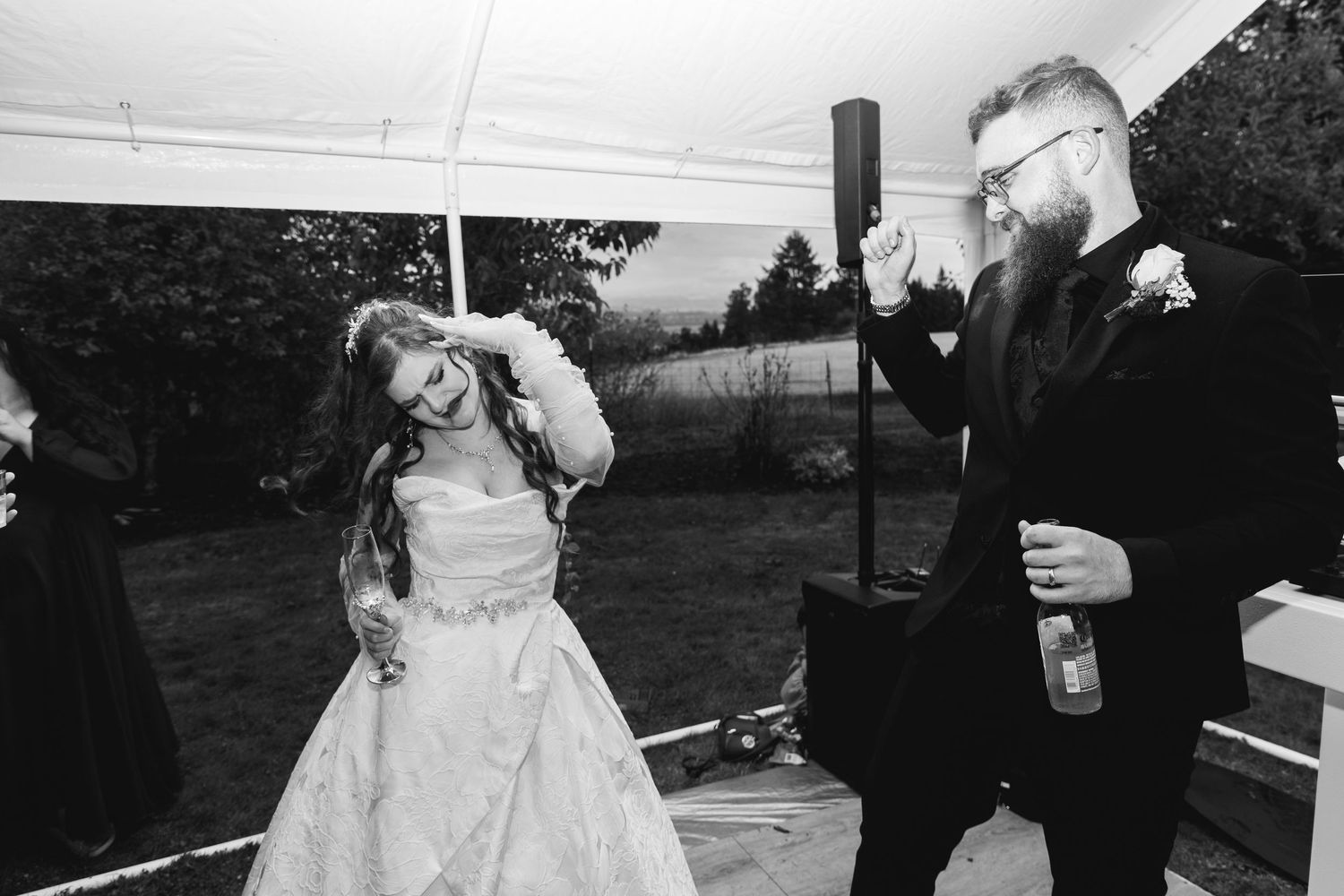 Black and white photo of bride and groom dancing joyfully at their wedding reception under a tent.