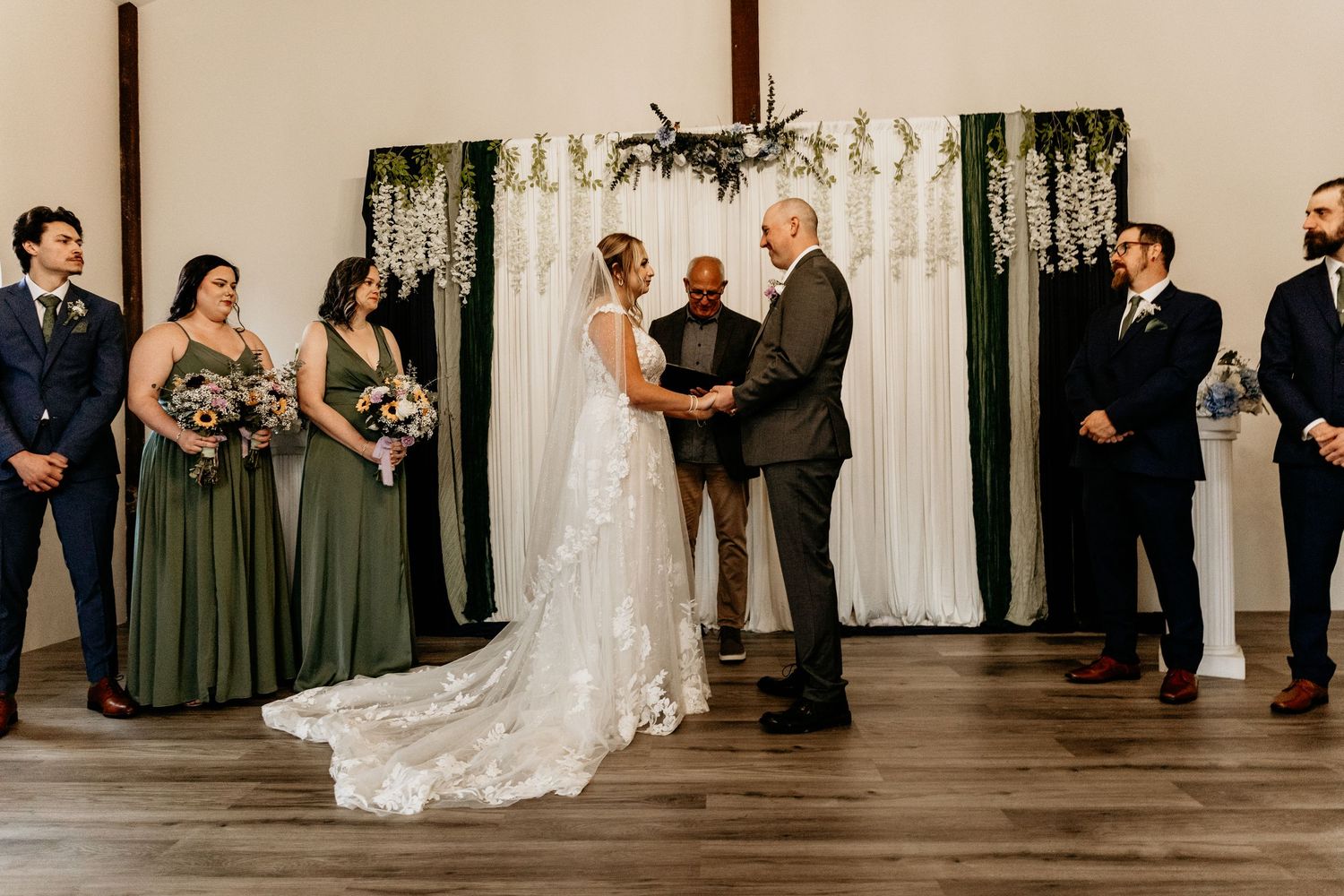 Bride and groom exchange vows at the altar flanked by bridesmaids in sage green and groomsmen in navy.