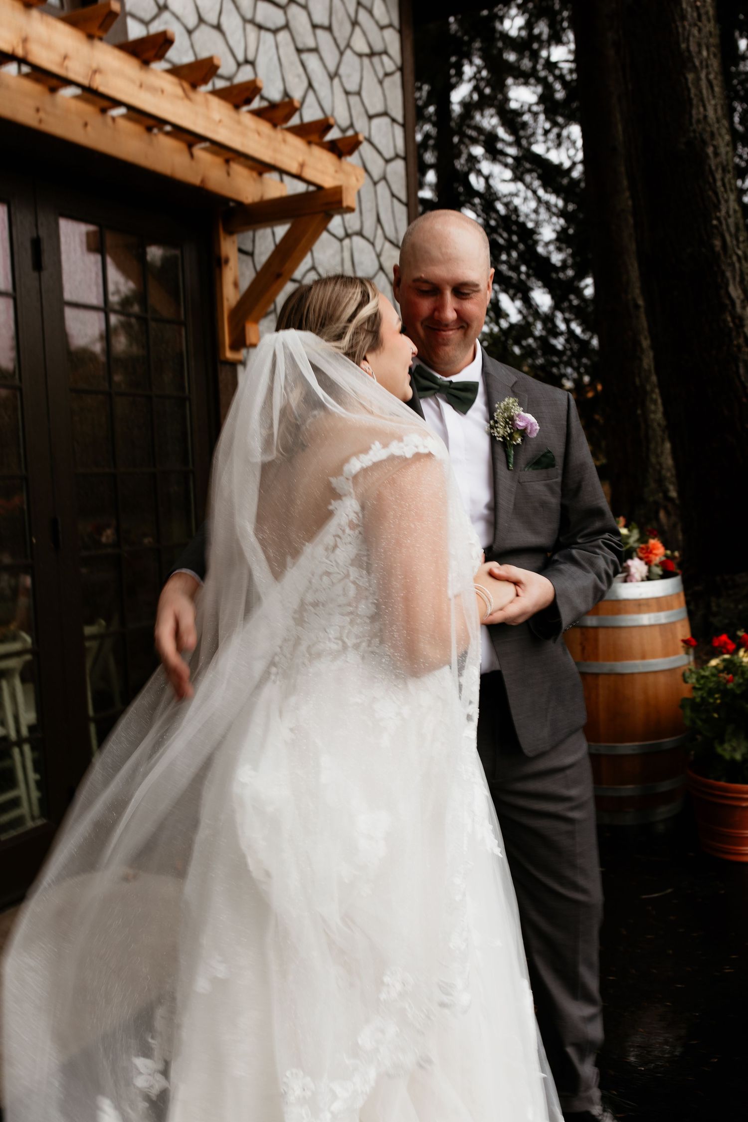 Smiling groom holds bride's hands outside rustic stone wedding venue.