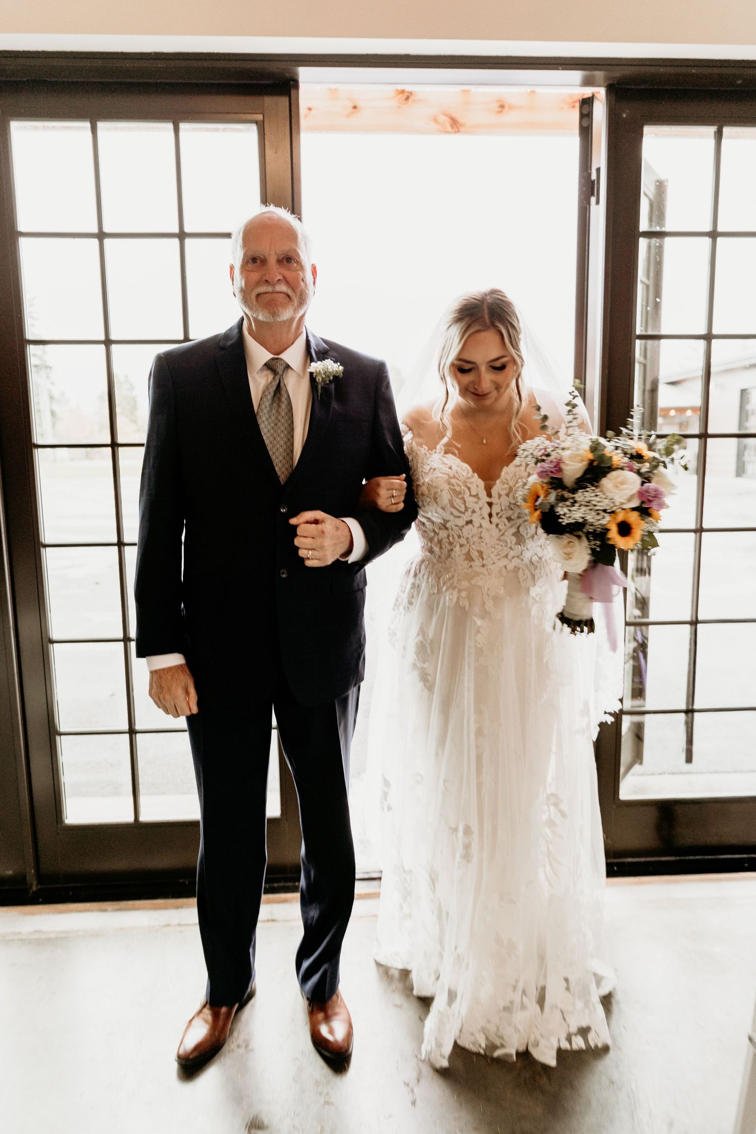 Father of the bride escorts his daughter down the aisle holding a colorful bridal bouquet.
