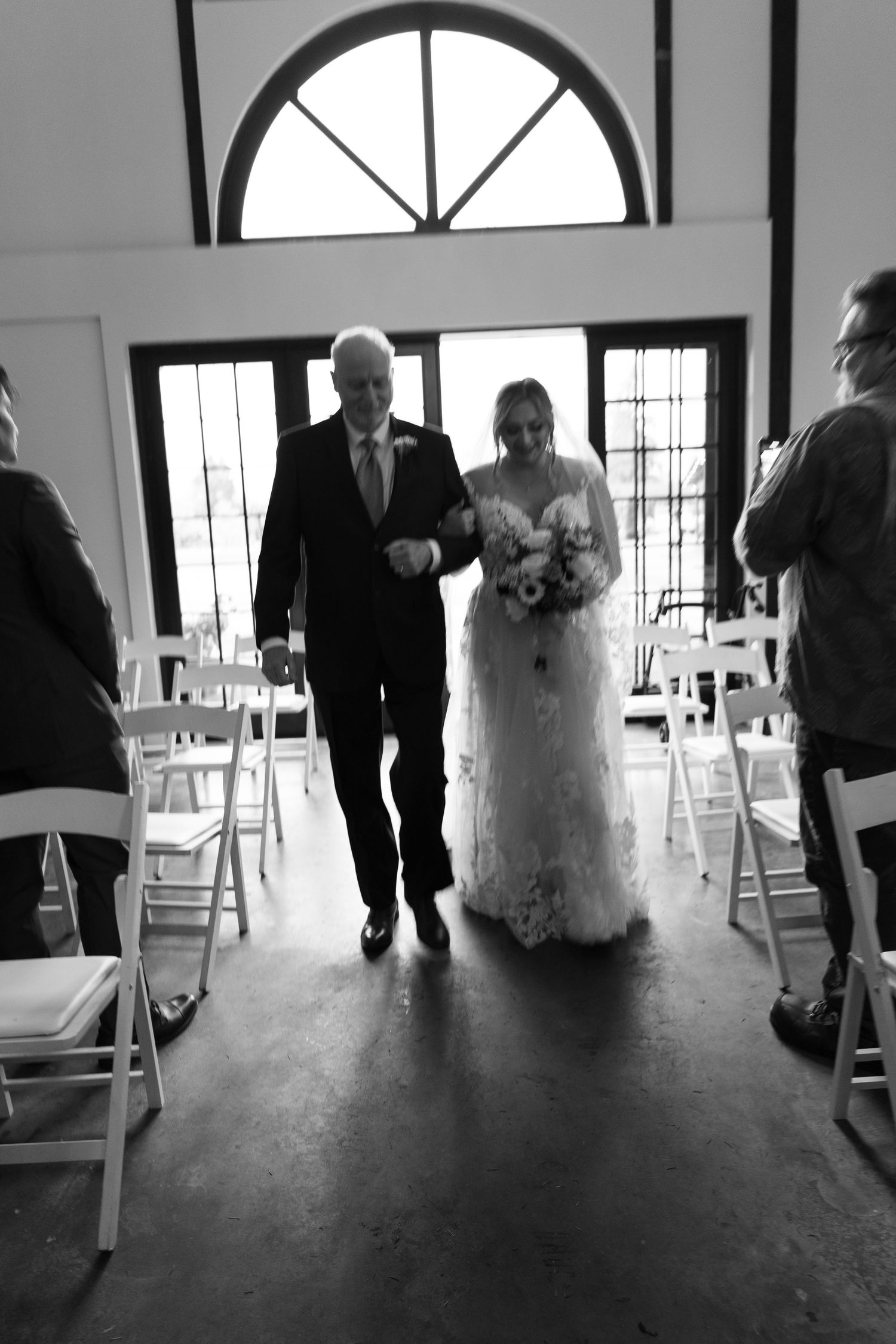 Black and white photo of a father walking his daughter down the aisle at a wedding ceremony.