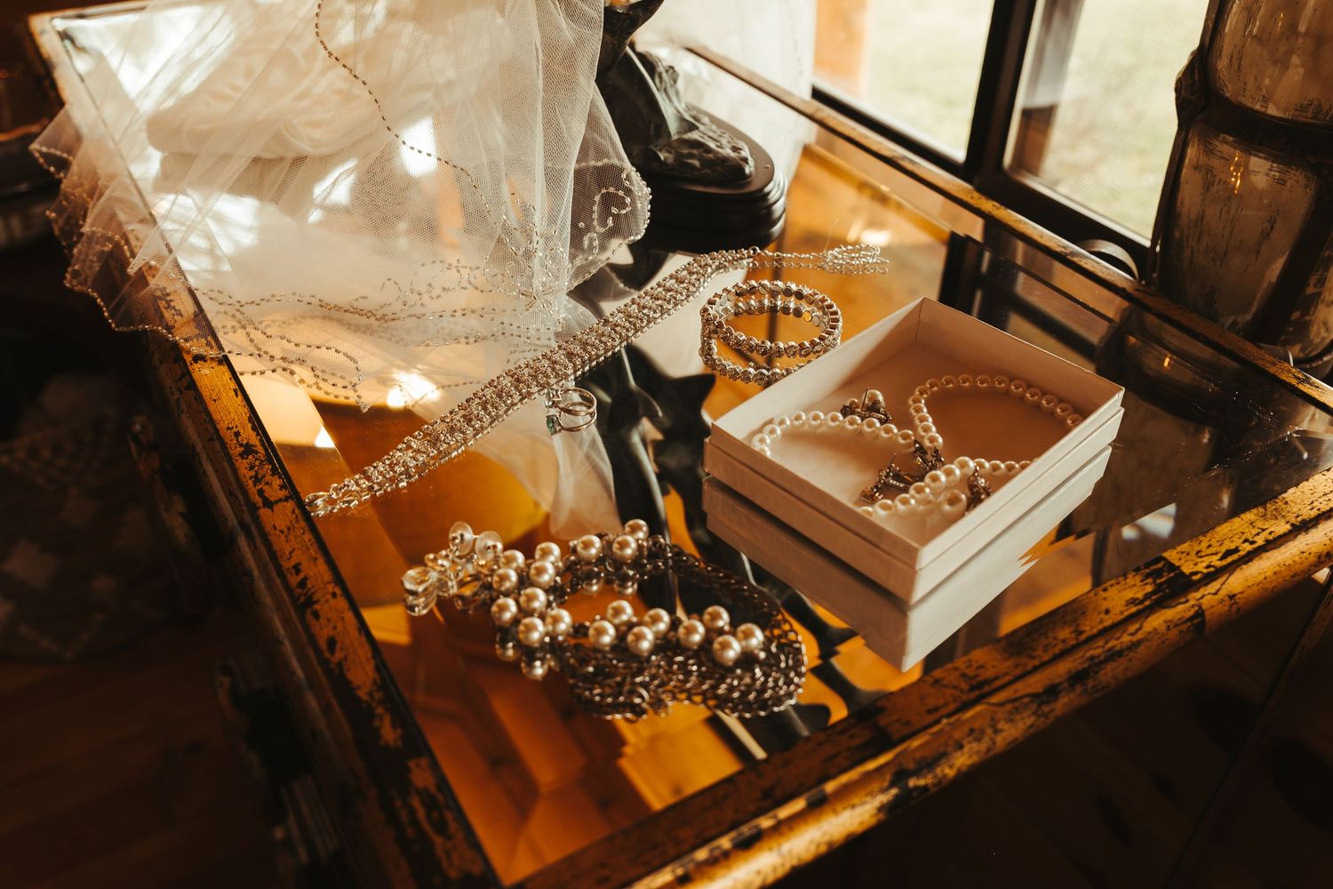 Elegant bridal jewelry display featuring pearl bracelets, crystal accessories, and a white gift box on a glass table.