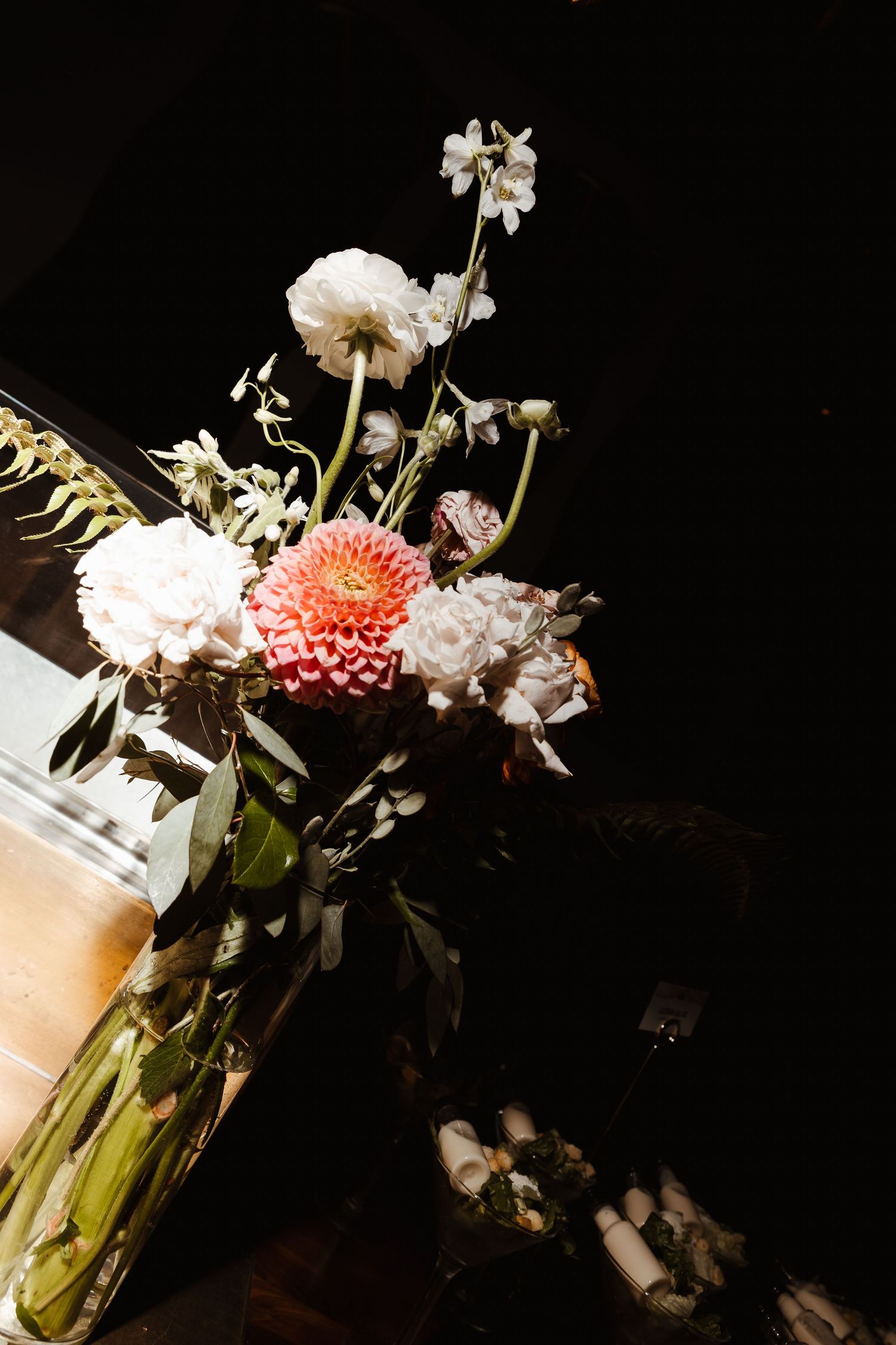 Elegant floral arrangement with white and coral dahlias in a glass vase against a dark background.