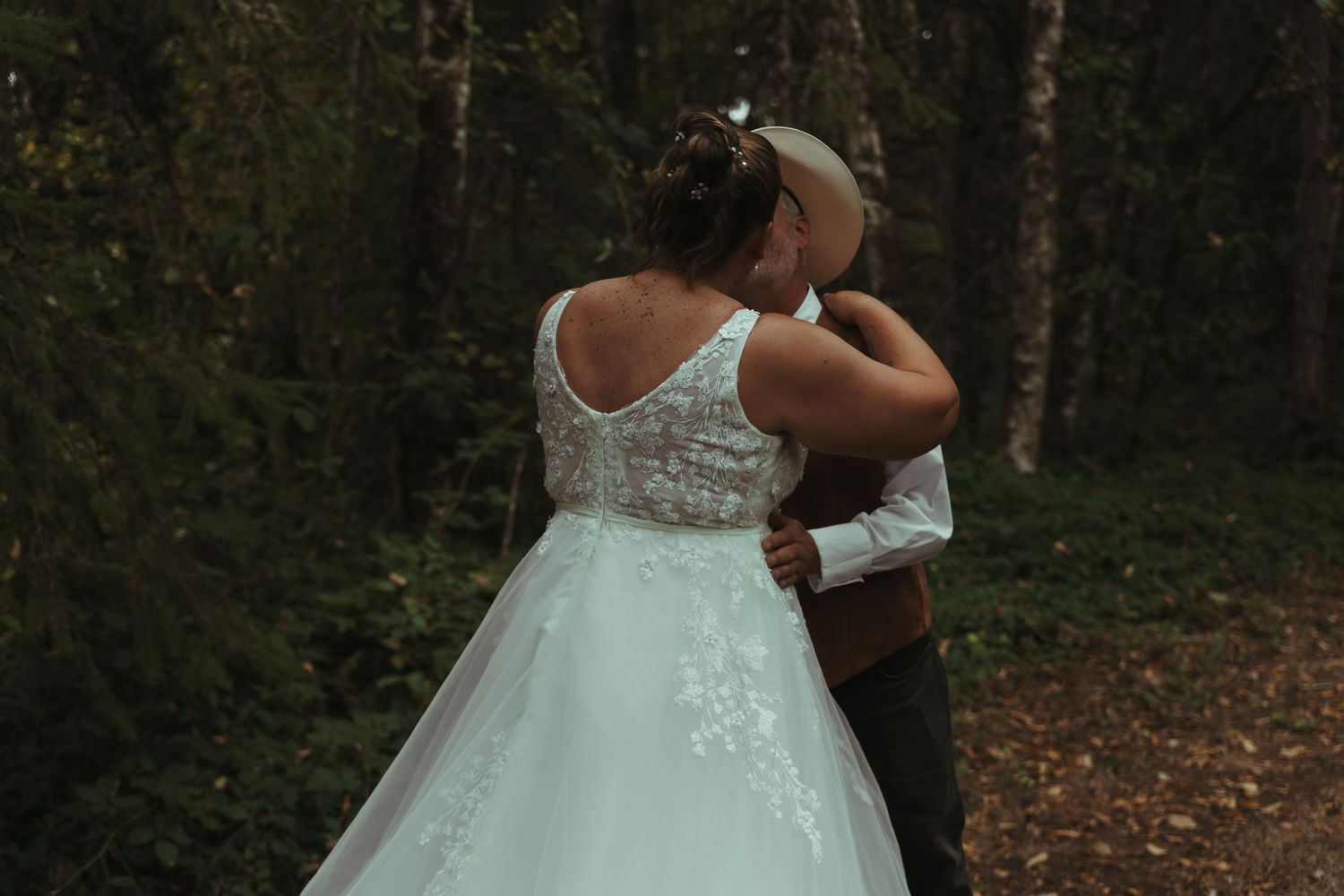 Bride and groom embracing in a lush green forest, sharing a tender moment.