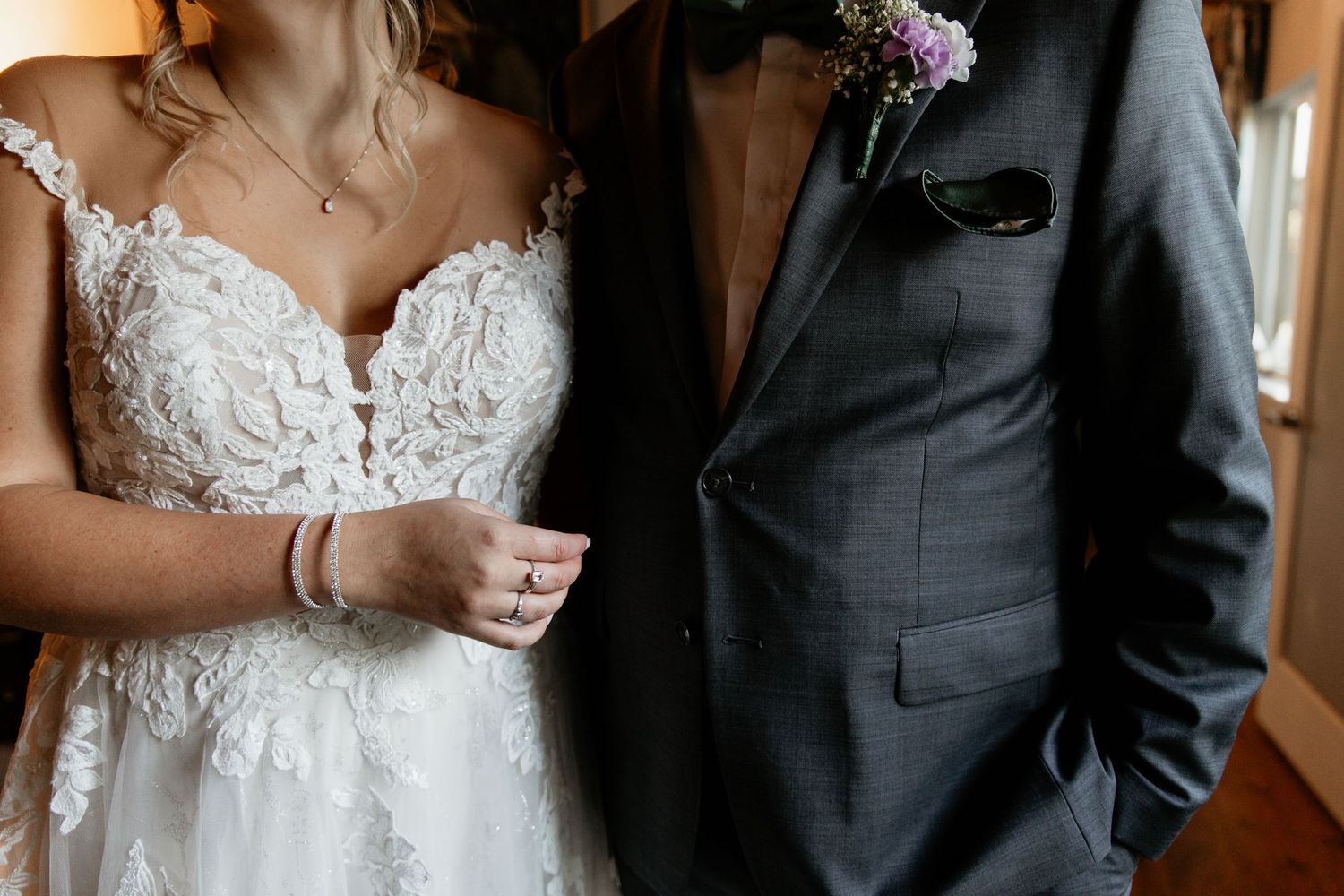 Close-up of bride in lace wedding gown and groom in gray suit holding hands on their wedding day.
