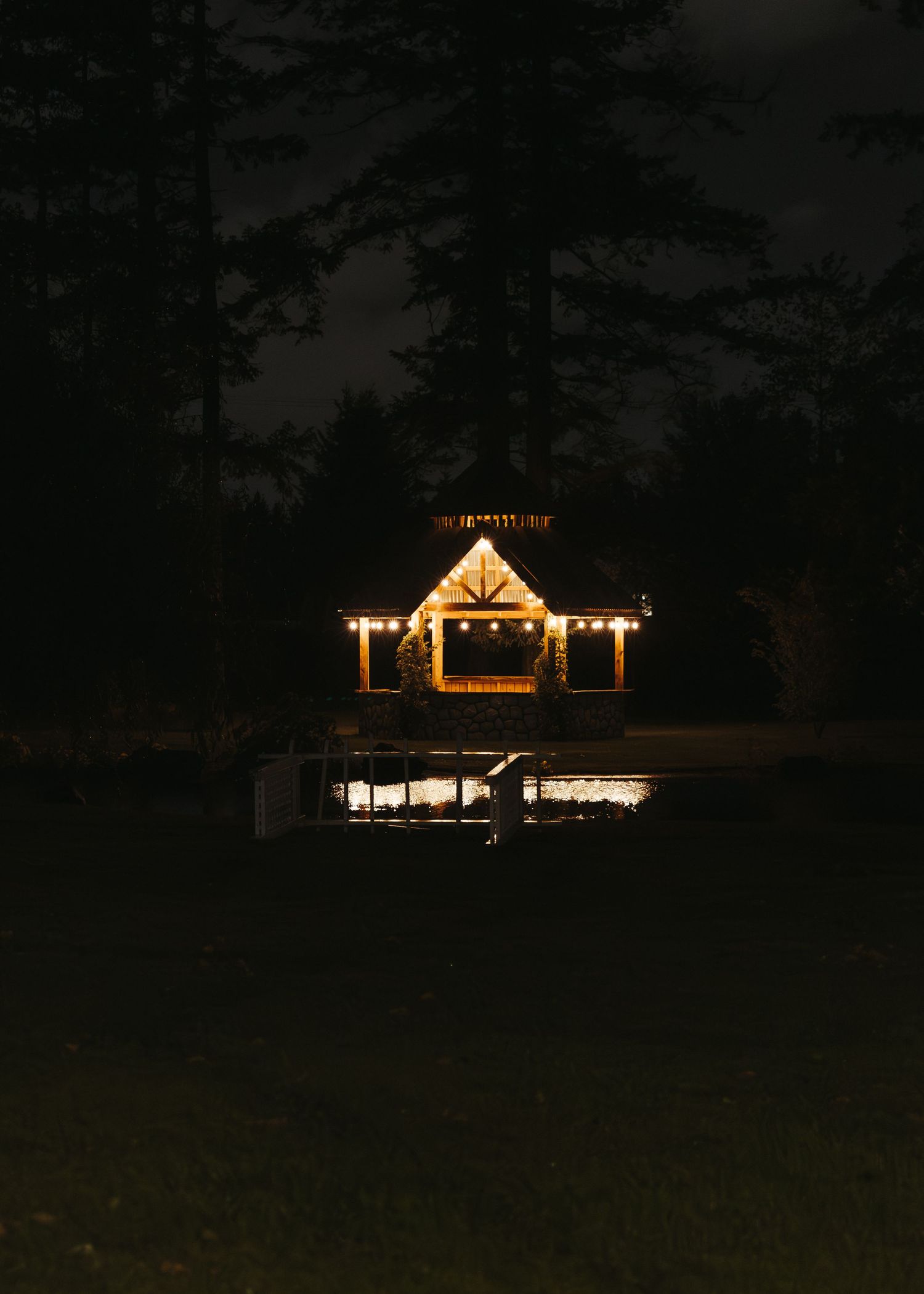 Warmly lit wedding venue pavilion surrounded by tall trees glowing beautifully against a dark night sky.