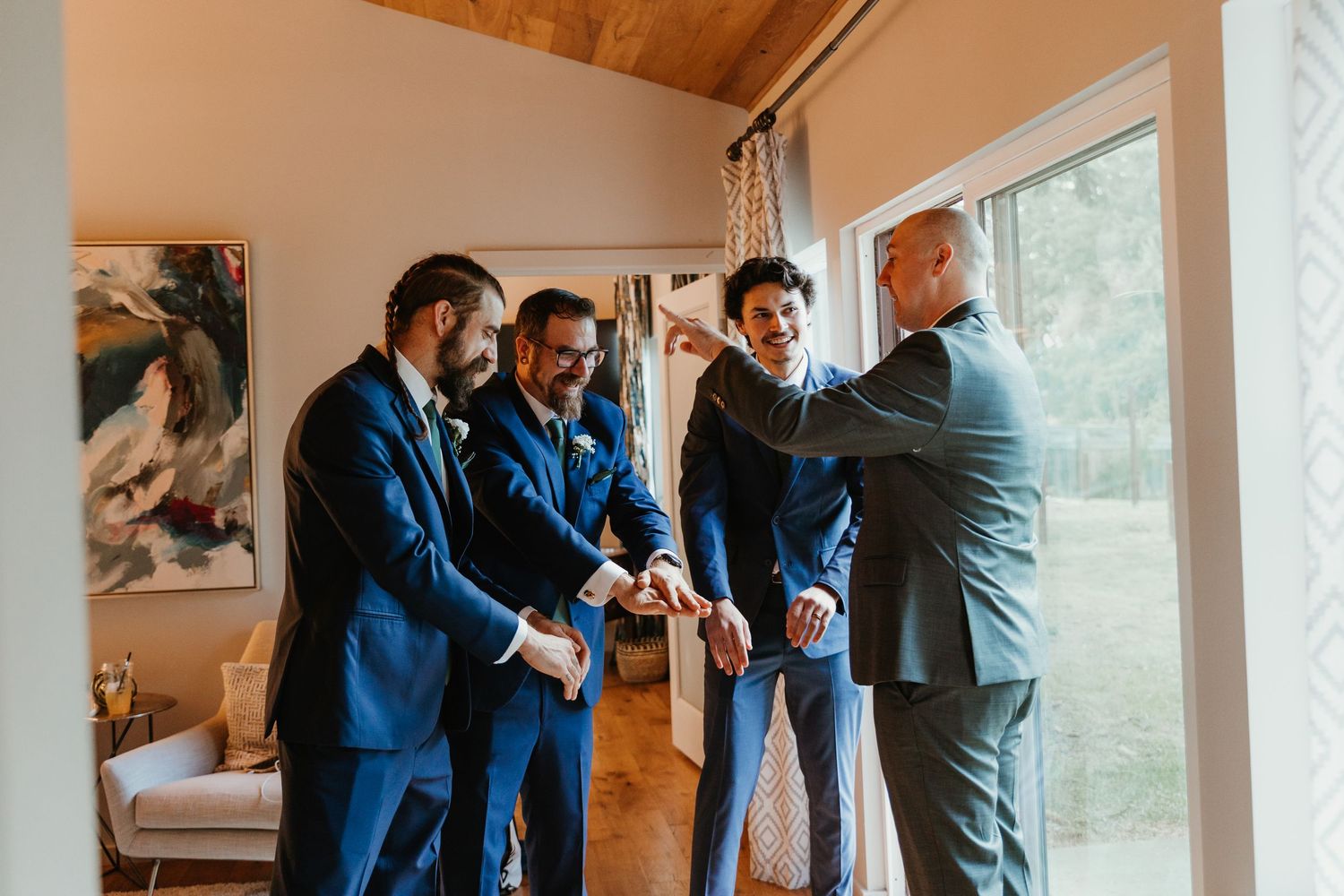 Groomsmen in navy suits sharing a celebratory moment together near a bright window before the wedding.