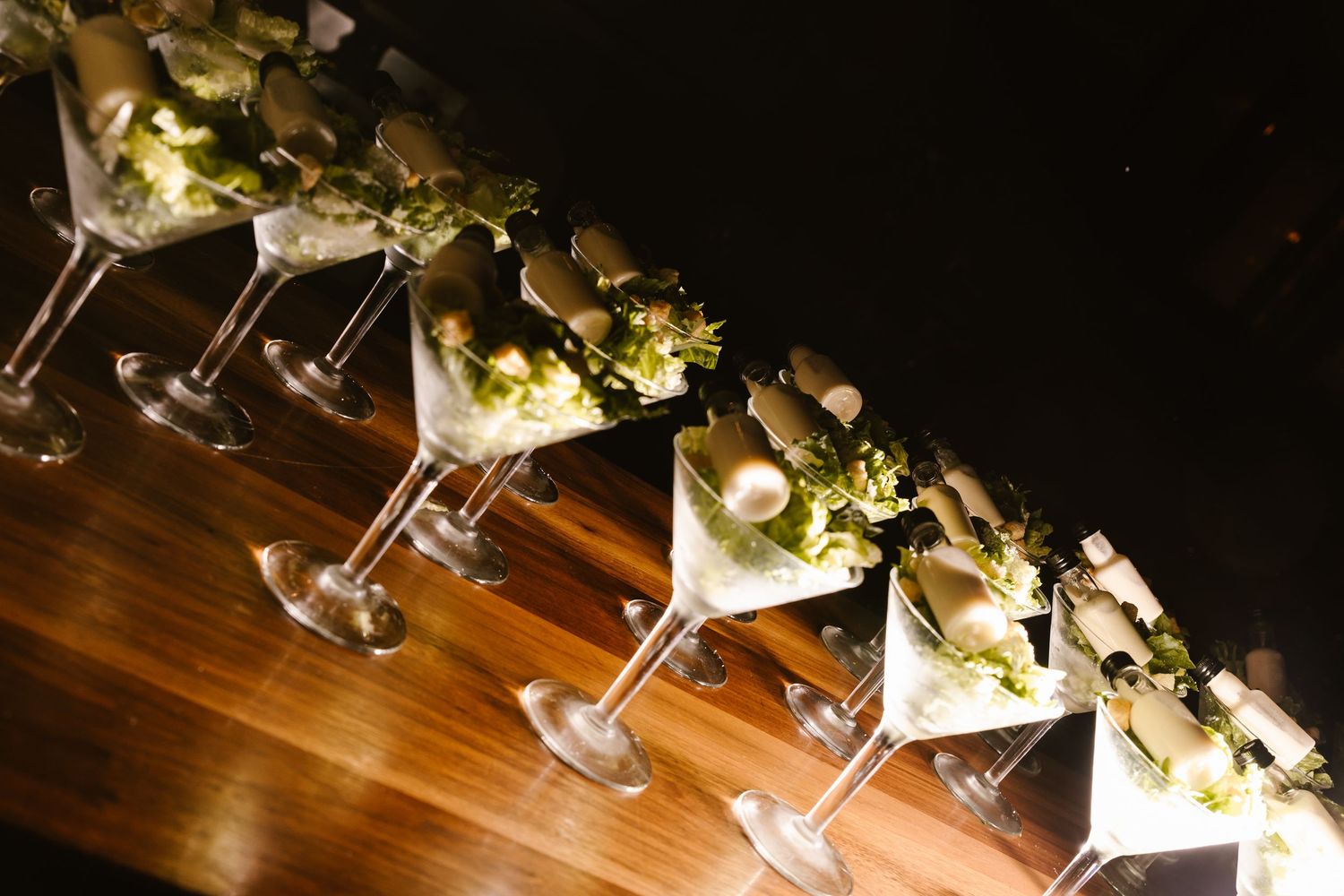 Row of elegant martini glasses garnished with flowers and herbs on a wooden bar, perfect for upscale events.