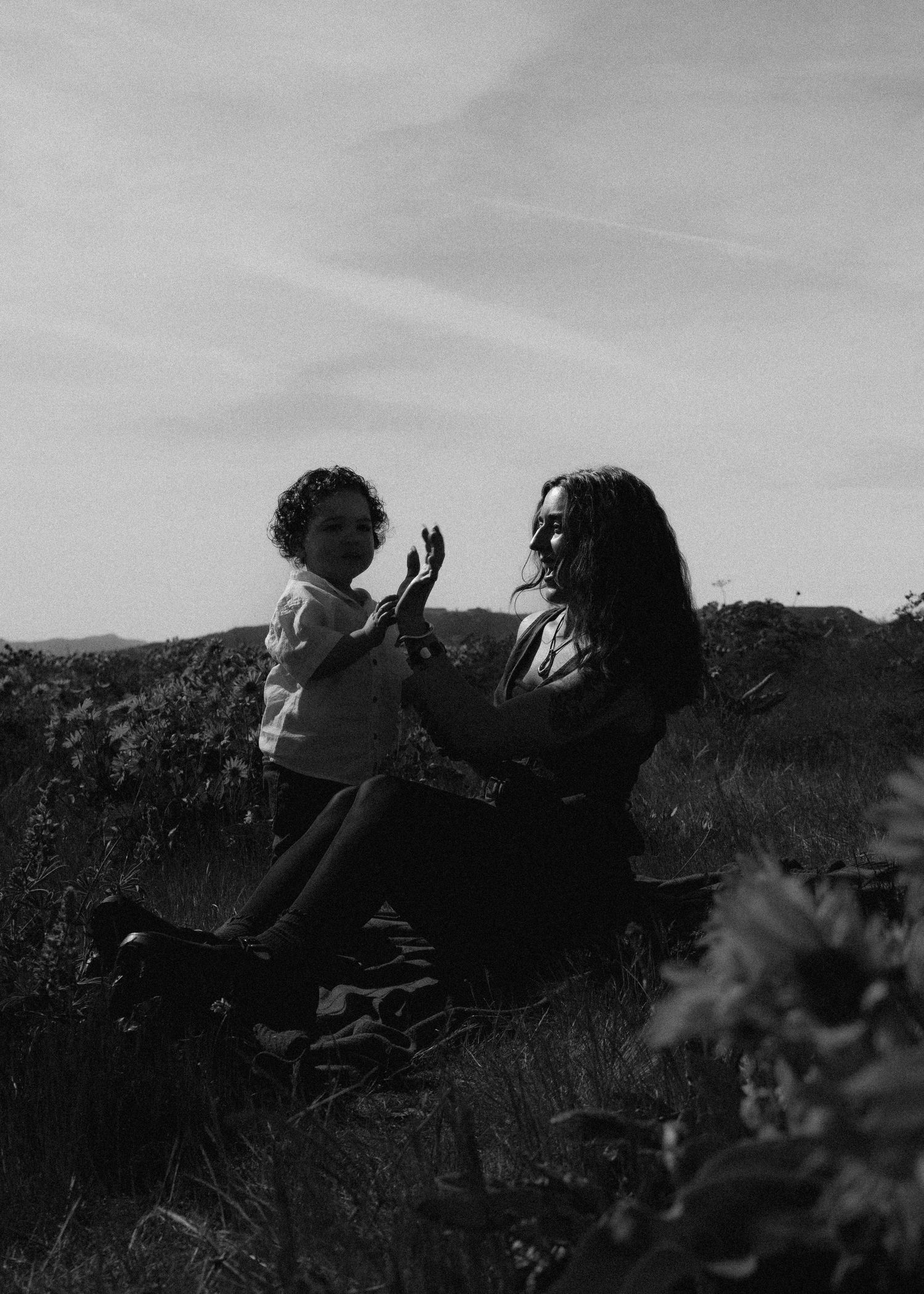 Black and white photo of a mother and young child sitting together in a field, sharing a tender moment outdoors.