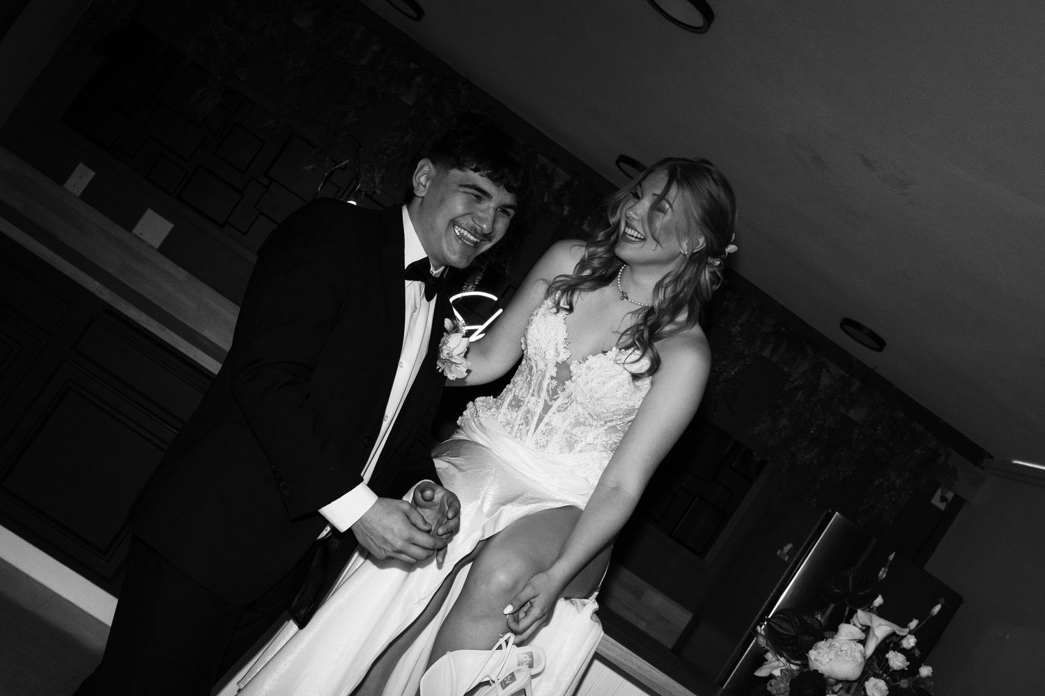 Black and white photo of a smiling couple in formal wedding attire, groom in tuxedo and bride in white gown.
