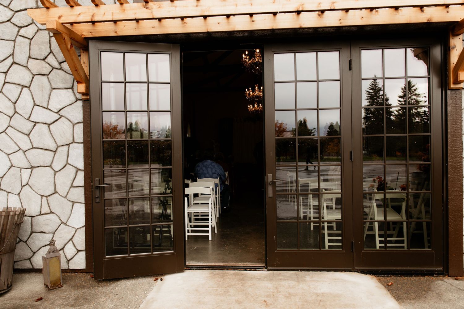 Elegant dark wood French doors opening to a wedding reception hall with white chairs and warm lighting.
