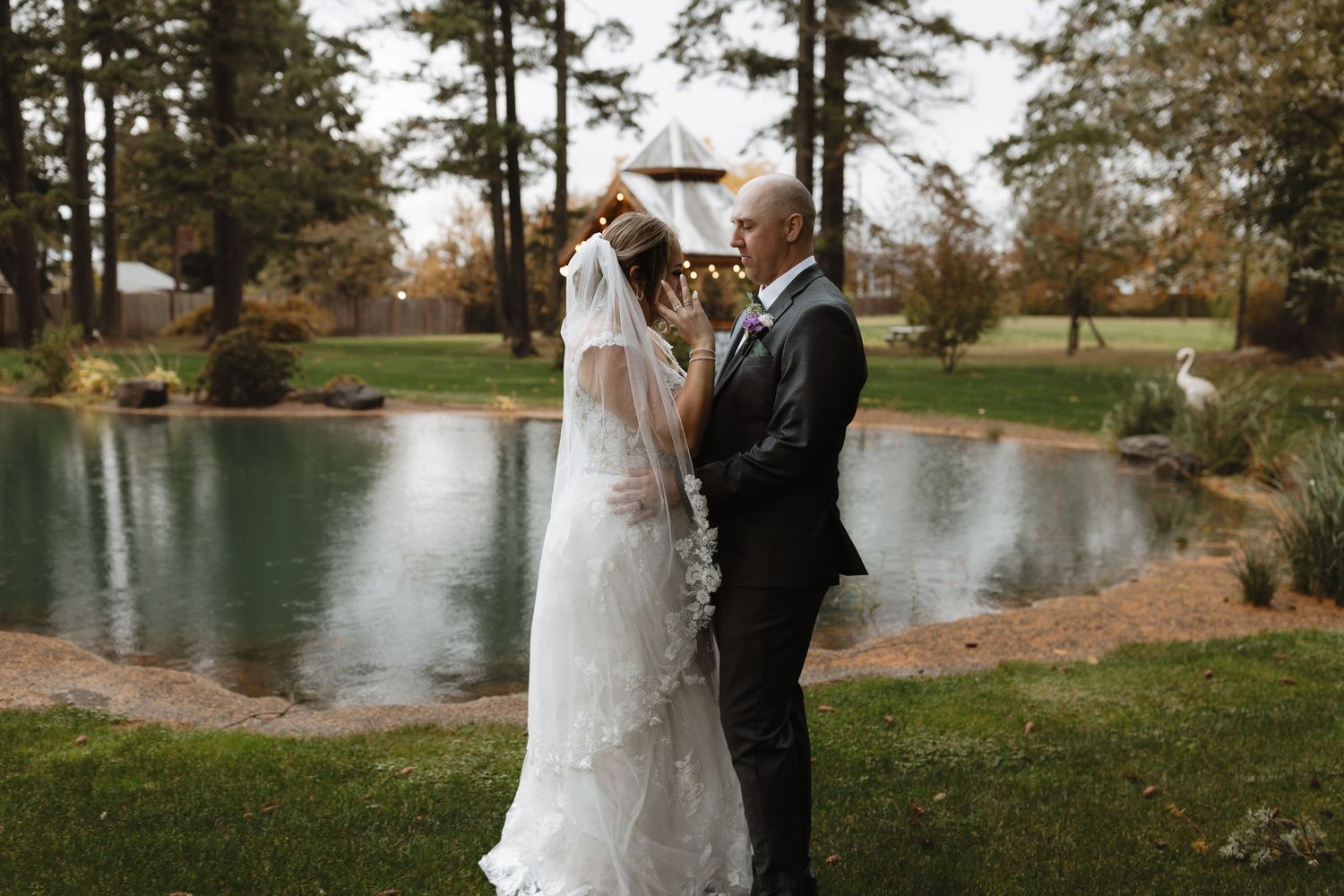 Bride and groom share a tender moment by a tranquil wedding pond.