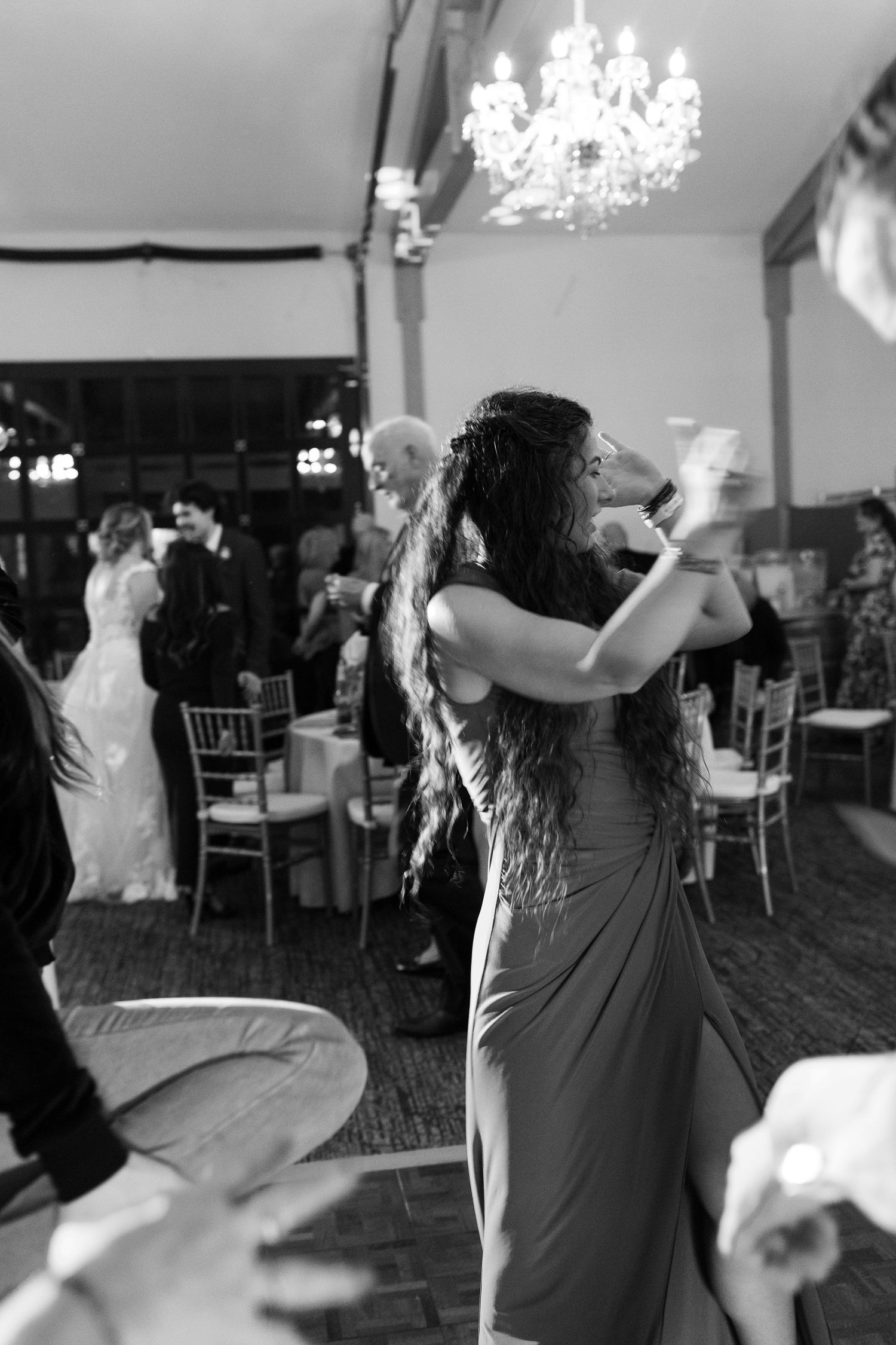 Wedding guest in elegant gown dances under a crystal chandelier at a reception venue.