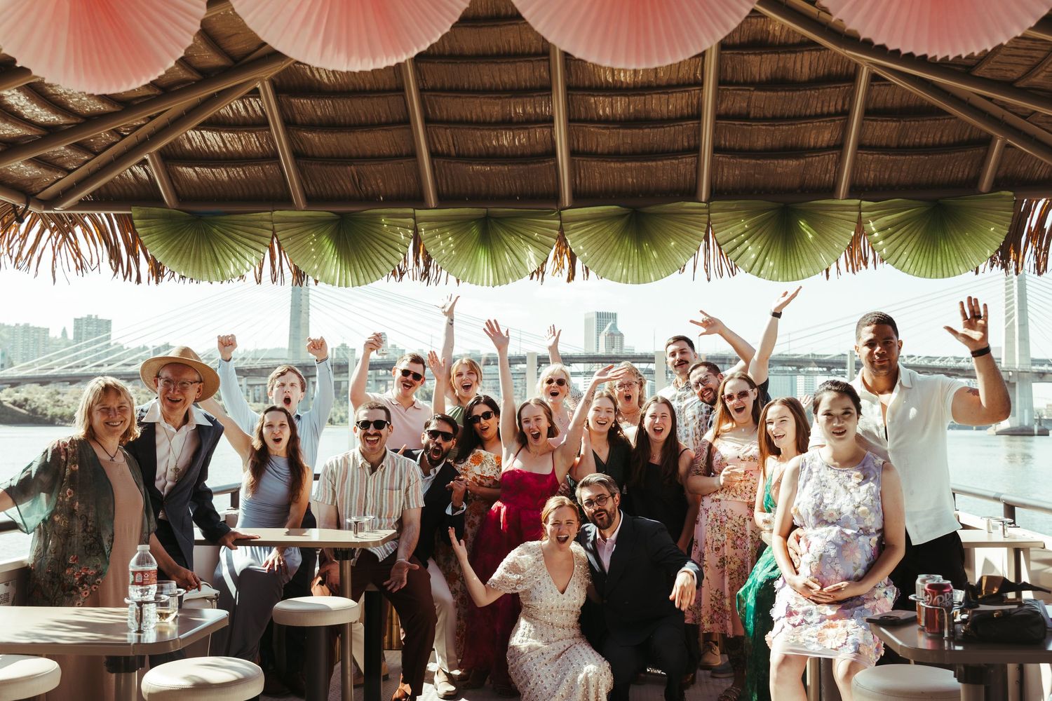 Group of wedding guests celebrating on a tropical tiki boat venue with city waterfront views.