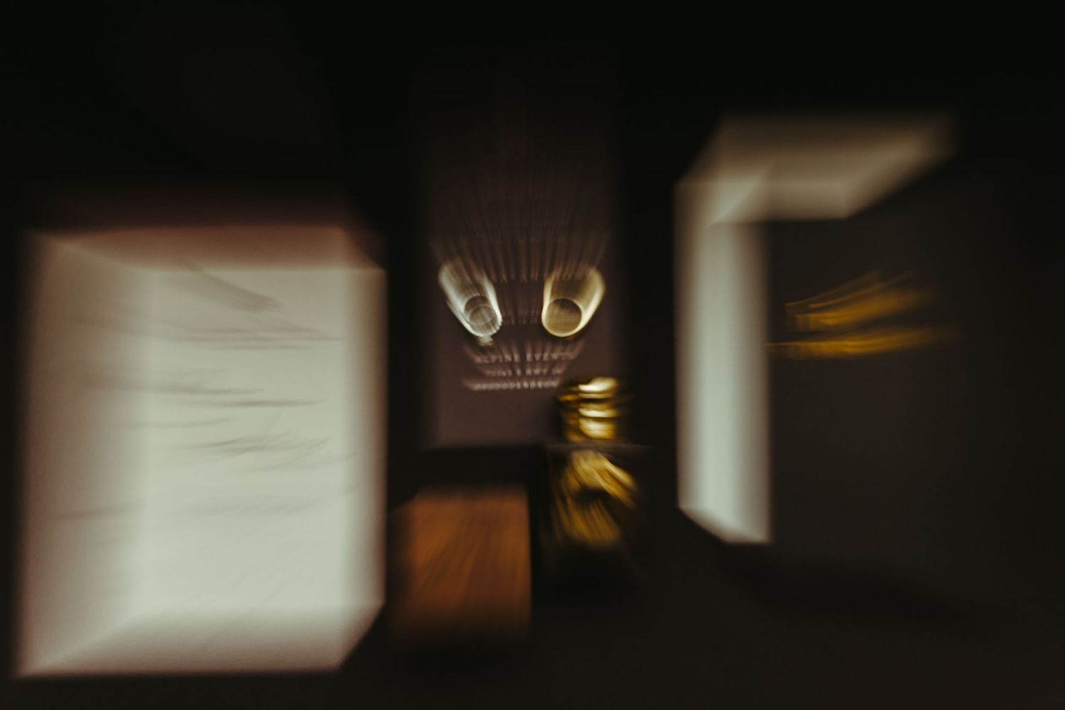 Blurred, abstract long-exposure photo of a dark room with glowing white light panels and warm golden lights creating dreamy motion streaks.
