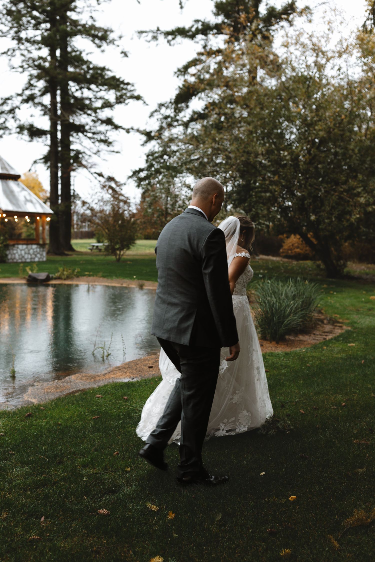 Bride and groom walk hand in hand along a scenic pond pathway.