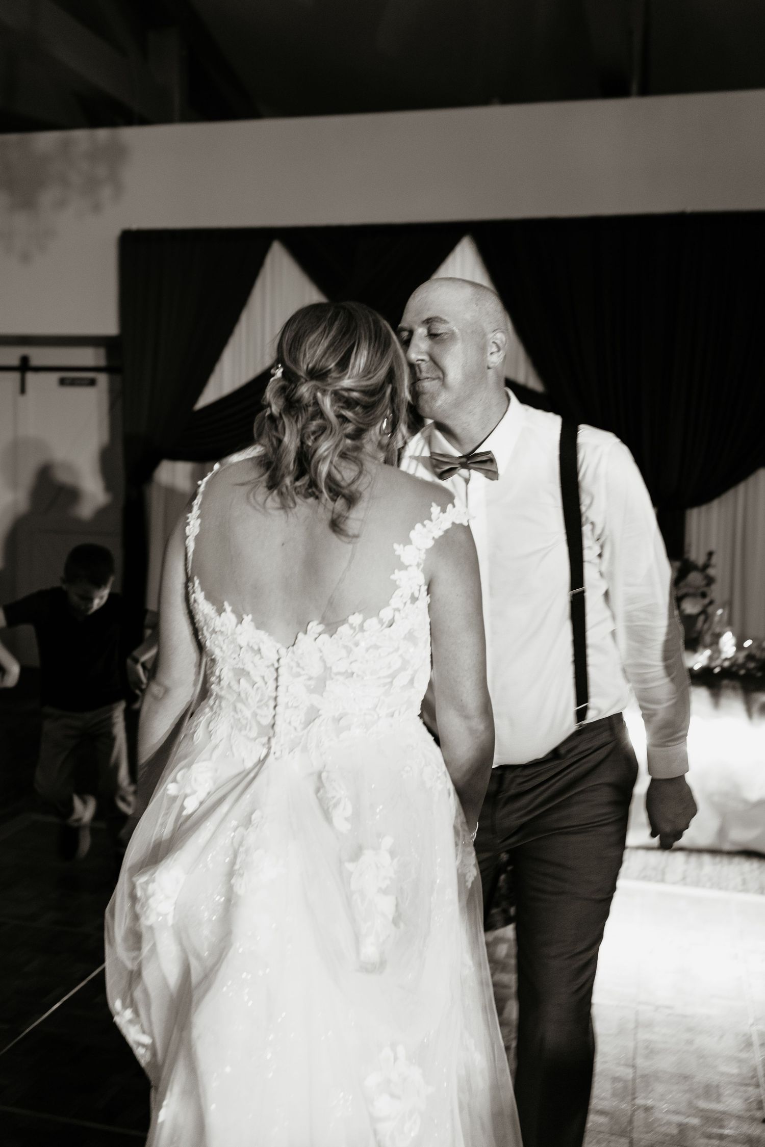 Bride in lace gown and groom in suspenders share an intimate moment on the wedding dance floor.